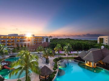 a pool with palm trees and a building with a beach and a sunset