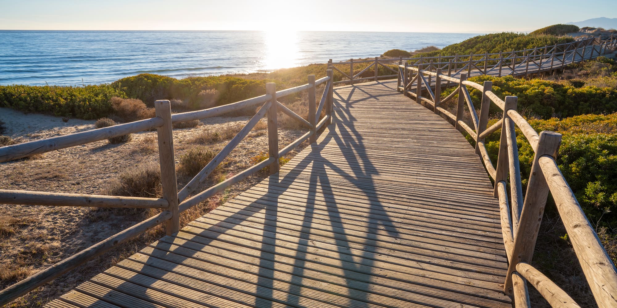 a wooden walkway with railings and a beach