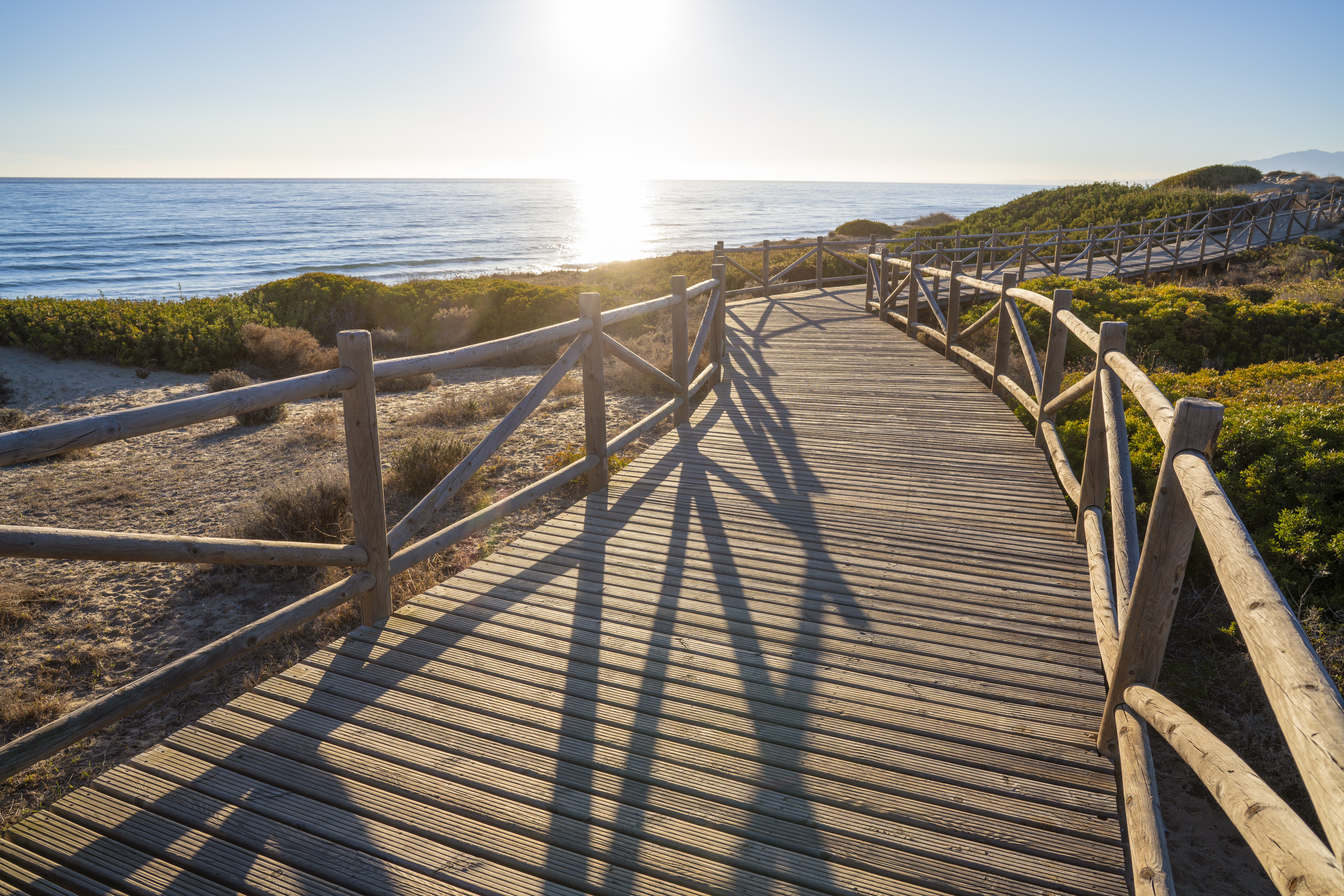 a wooden walkway with railings and a beach