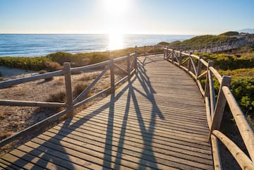 a wooden walkway with railings and a beach
