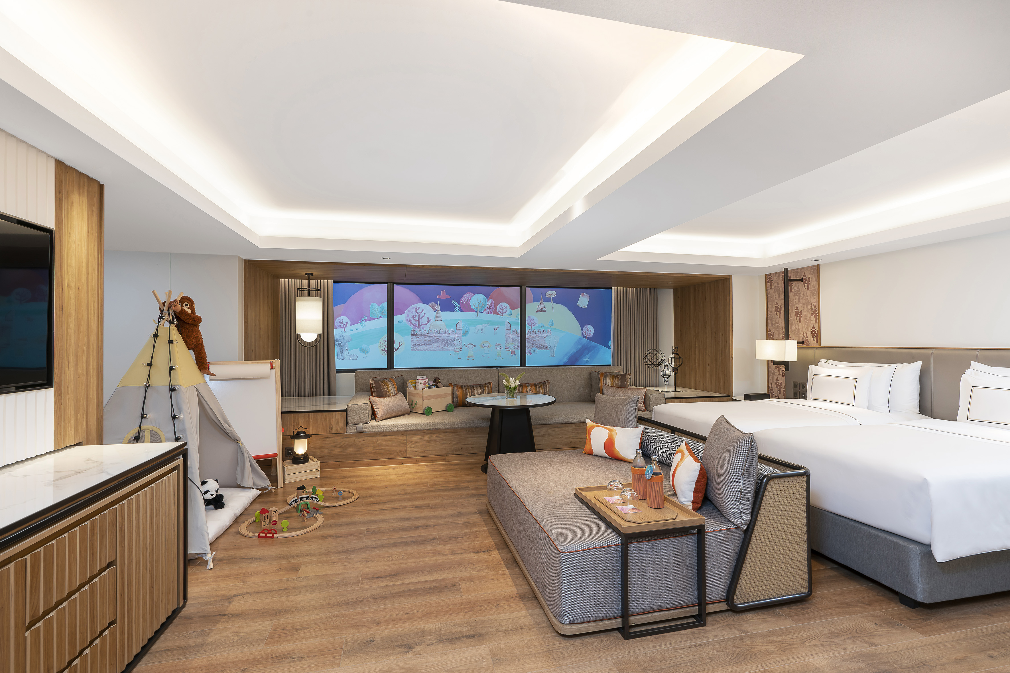 Family hotel suite with kids' play tent, toys, twin beds, and large screen.