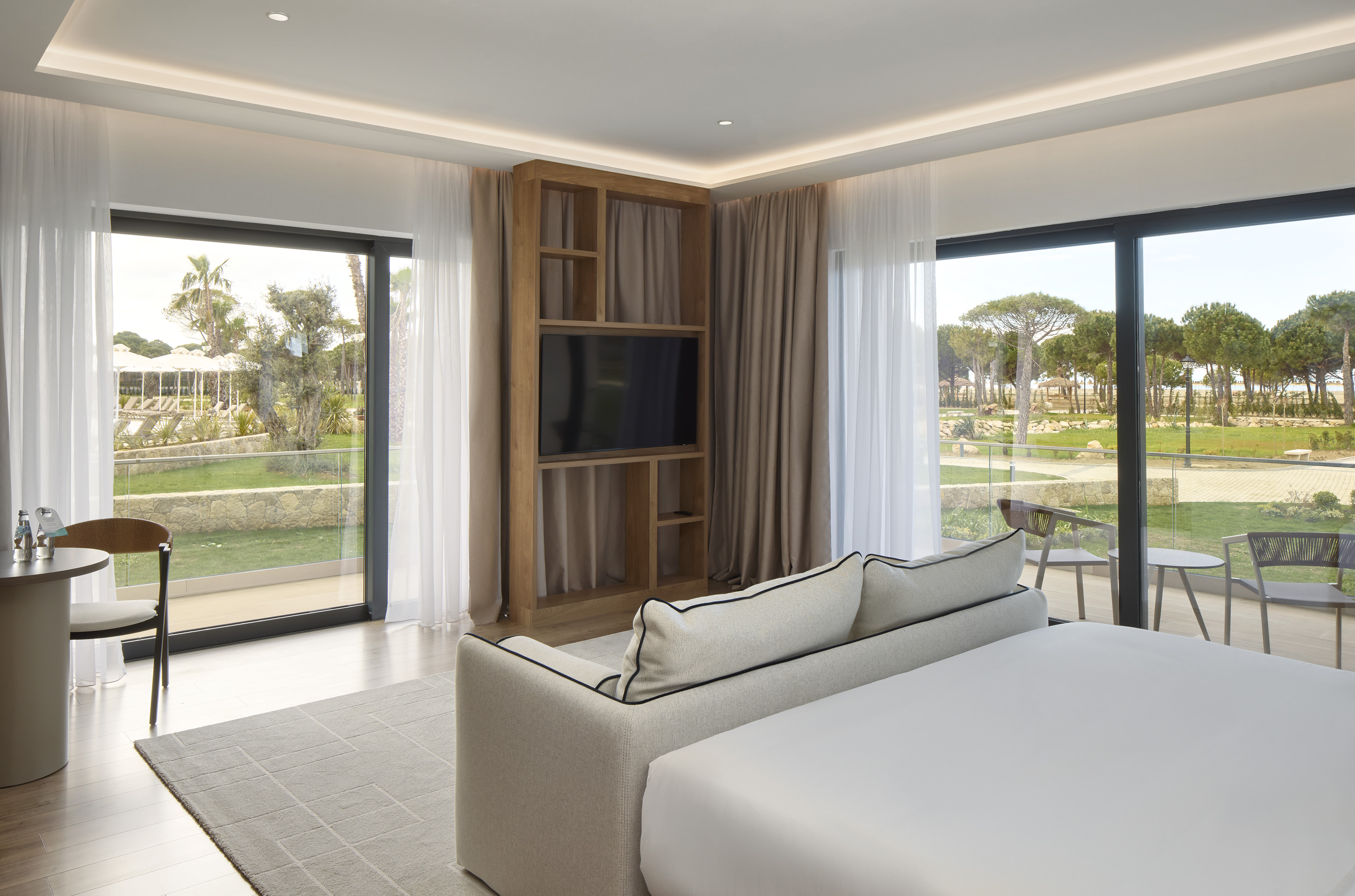 Modern hotel suite with bed, sofa, TV, and garden view patio.