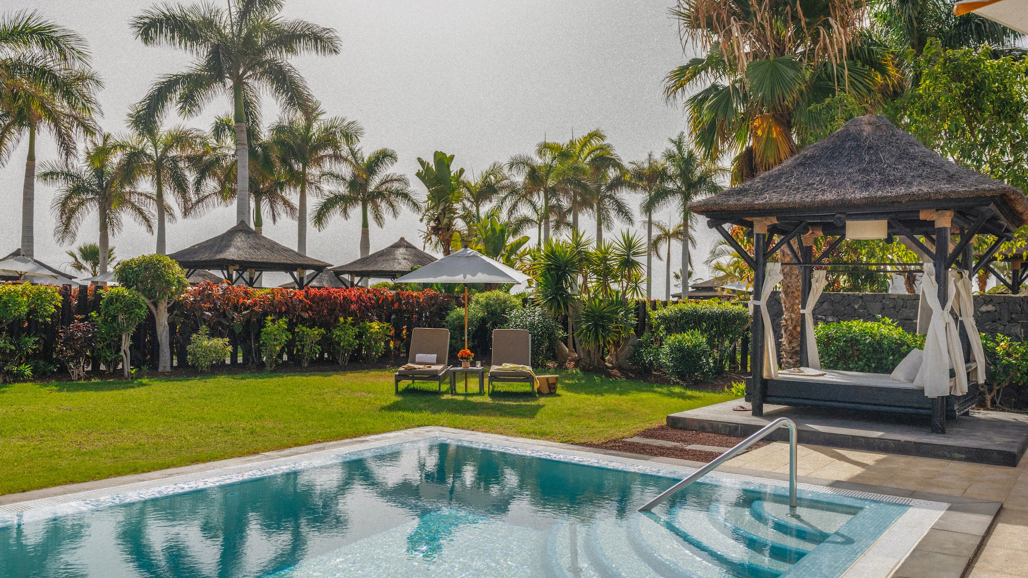 Private resort pool area with palm trees, sunbeds, and thatched cabana.