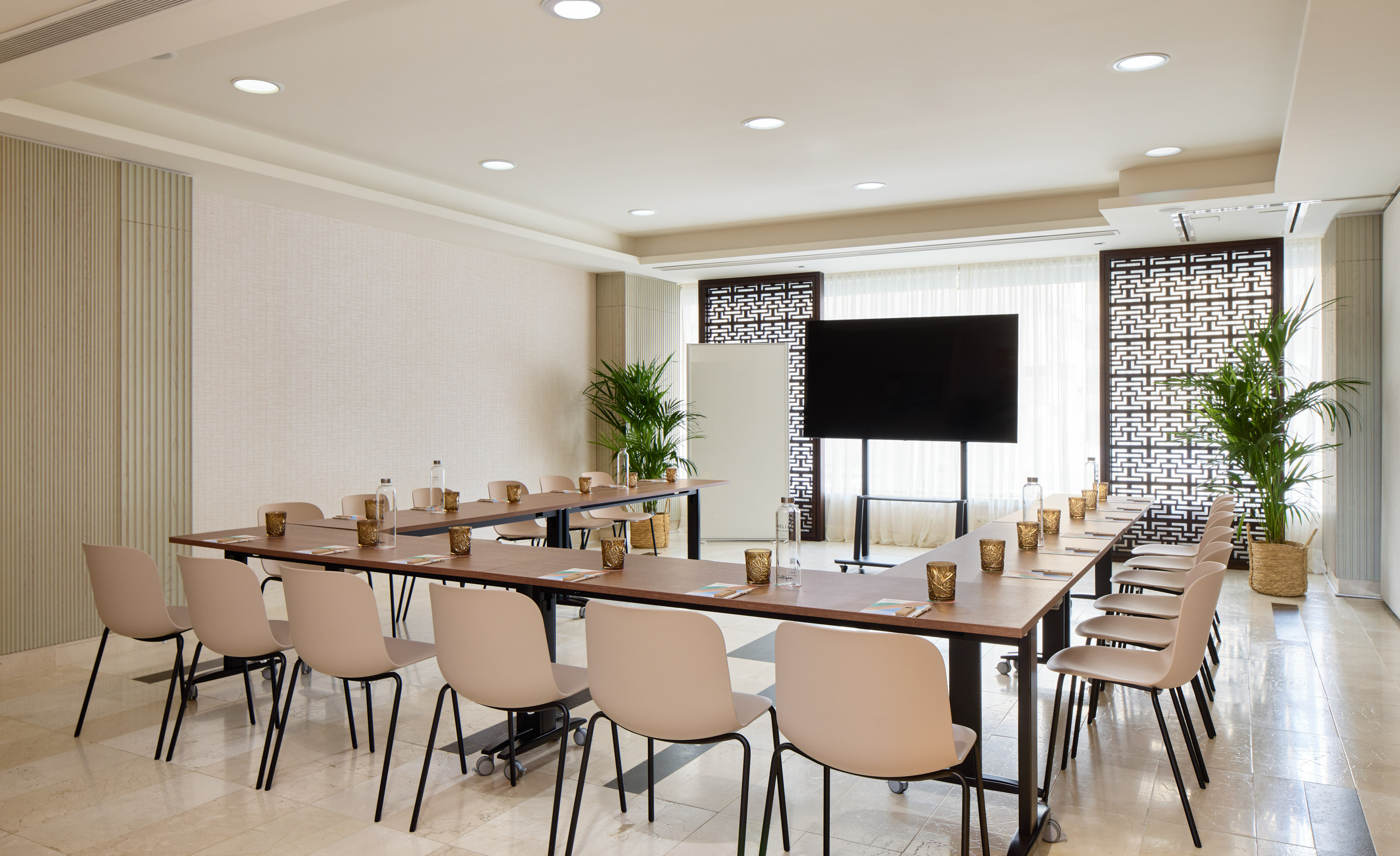 Modern U-shaped meeting room with light chairs, tables, and large screen.