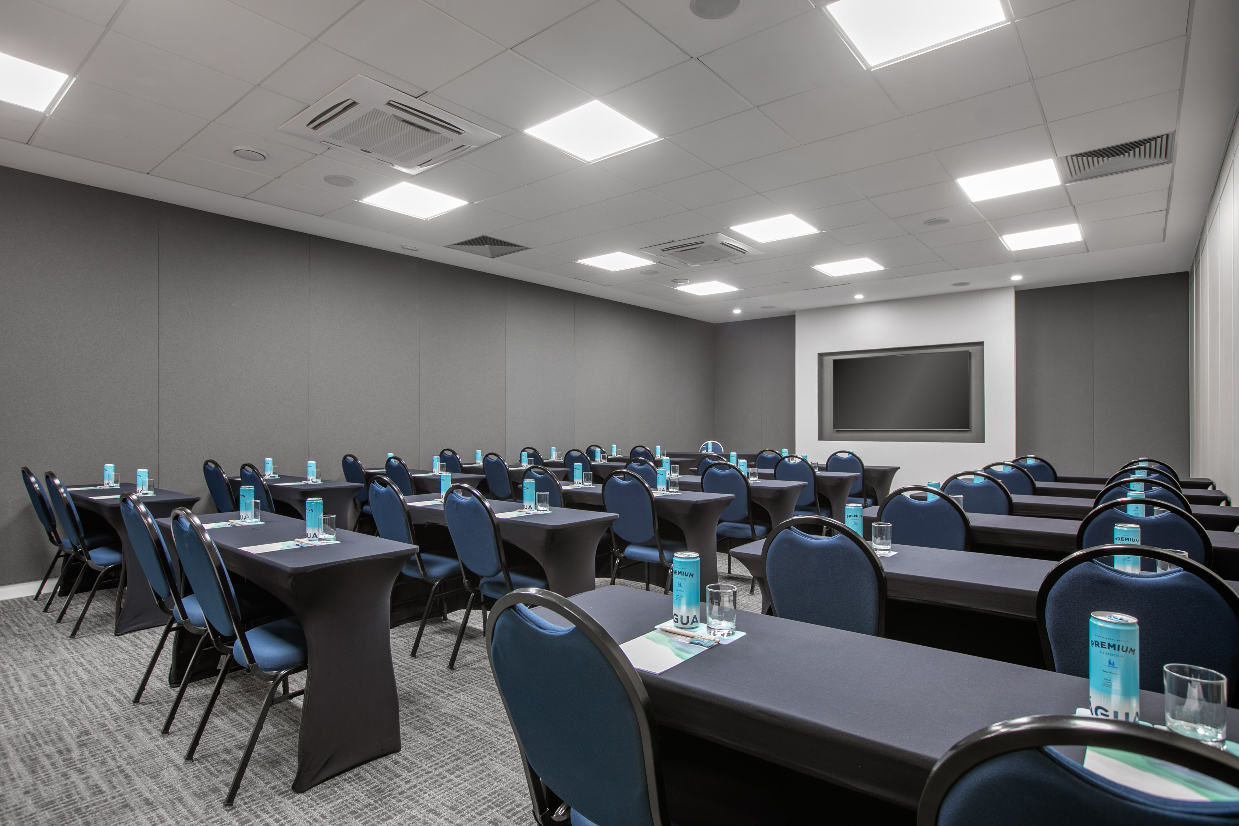 Modern meeting room with blue chairs, black tables, and a large TV display.