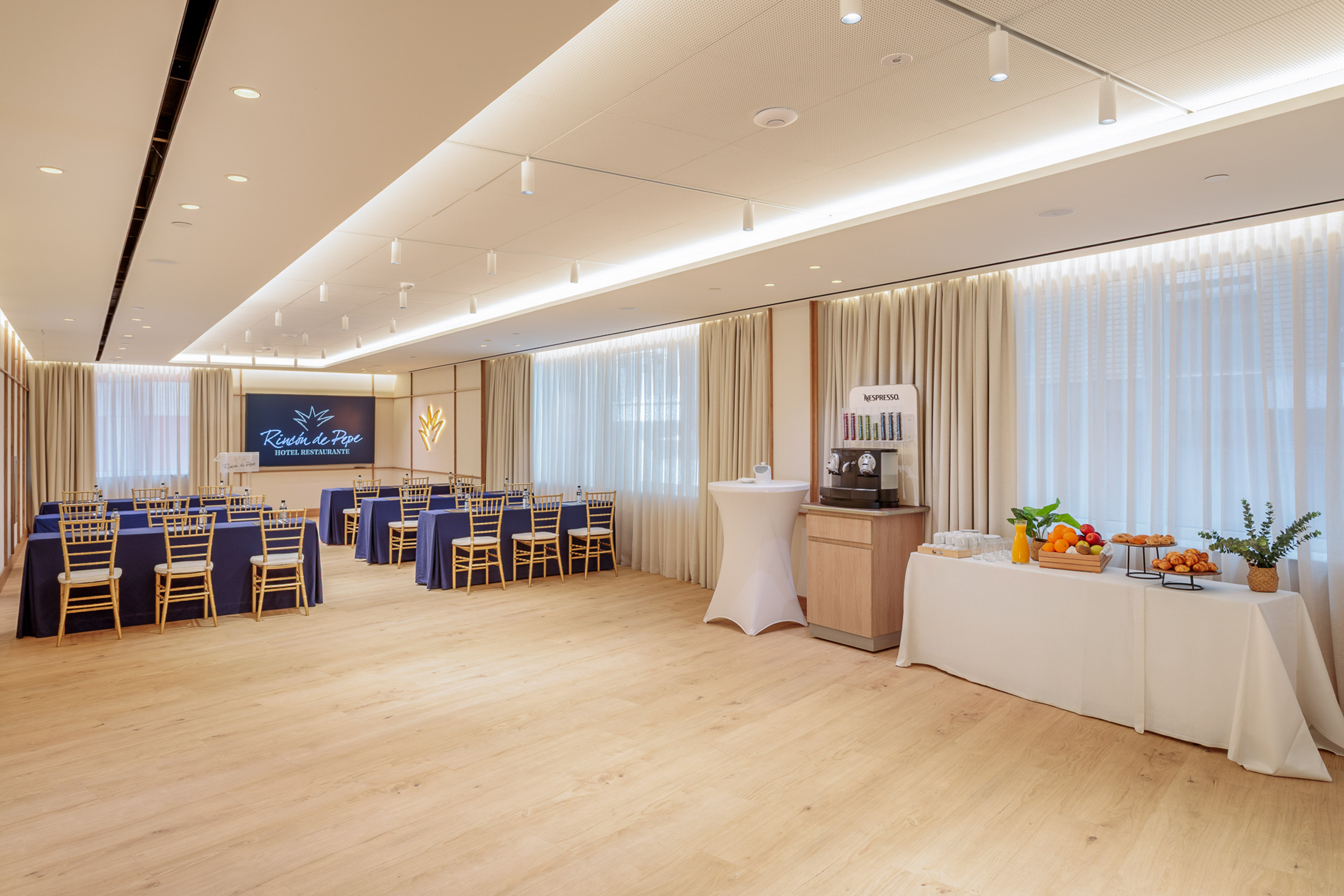 Meeting room with blue tables, golden chairs, Nespresso machine, and buffet.