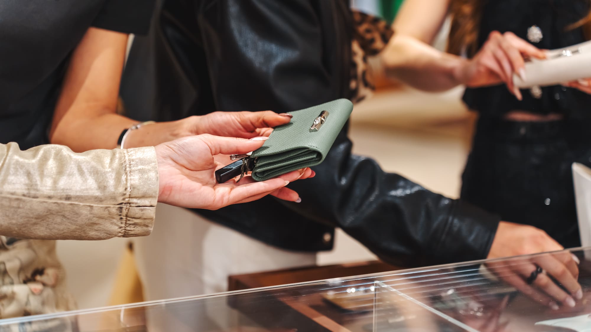 Hands holding a green wallet with a key fob over a store display case.