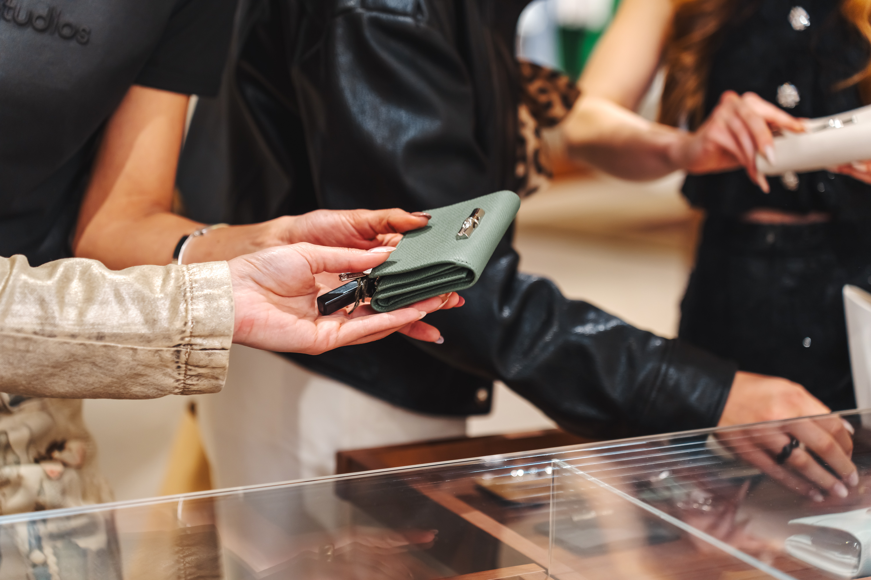 Hands holding a green wallet with a key fob over a store display case.