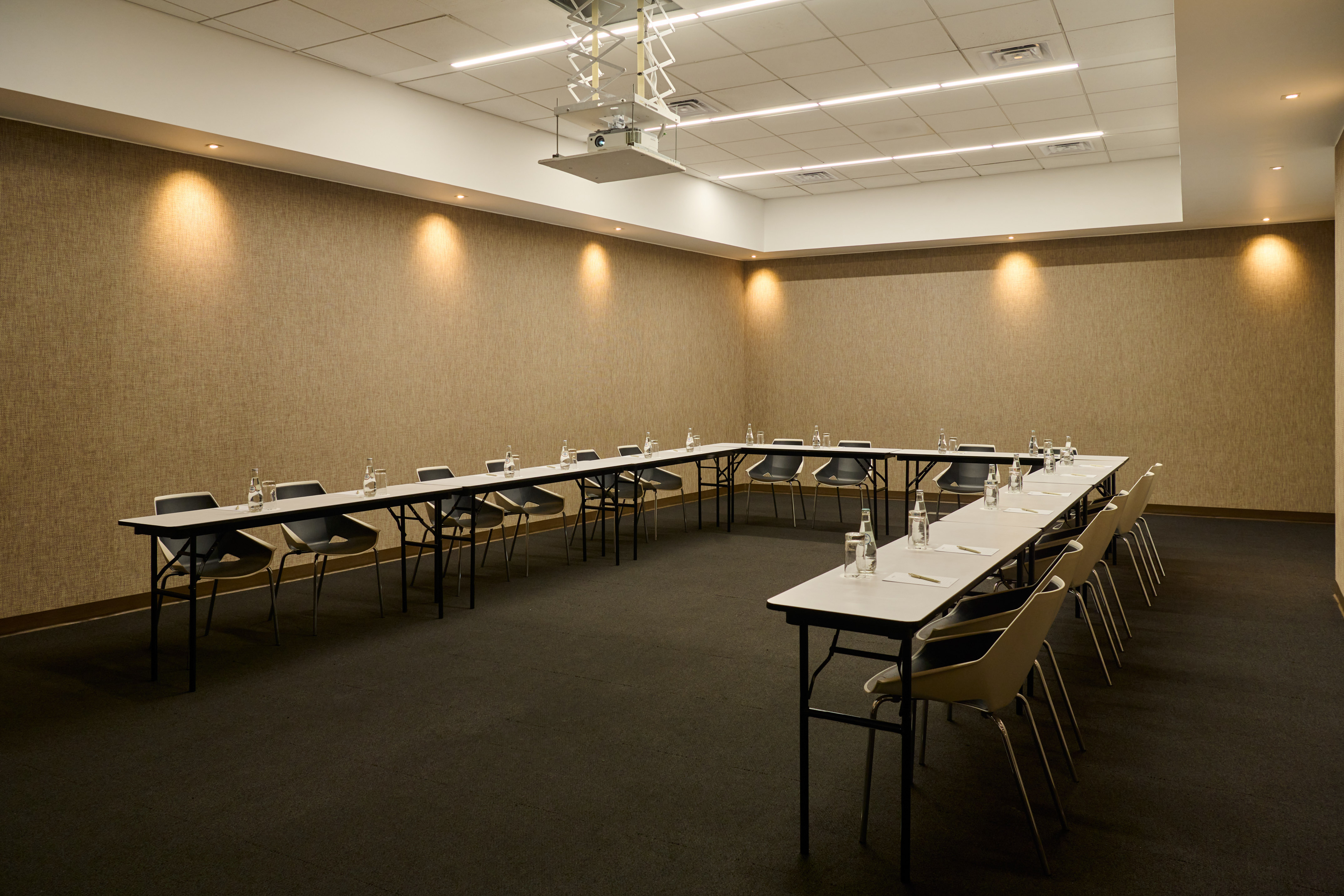U-shaped conference room setup with tables, chairs, water, and projector.