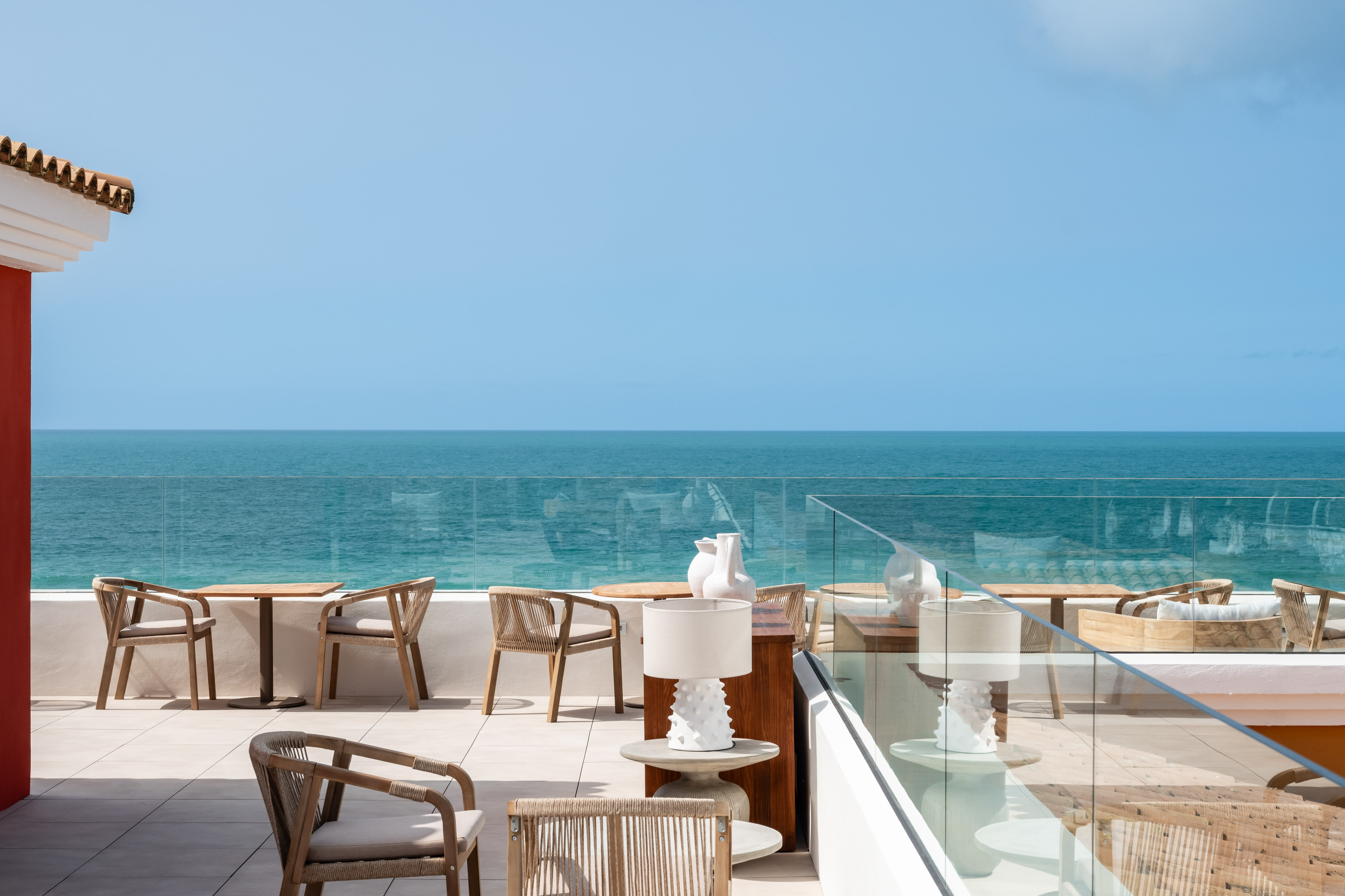 Sunny ocean view terrace with modern outdoor seating and glass railing.
