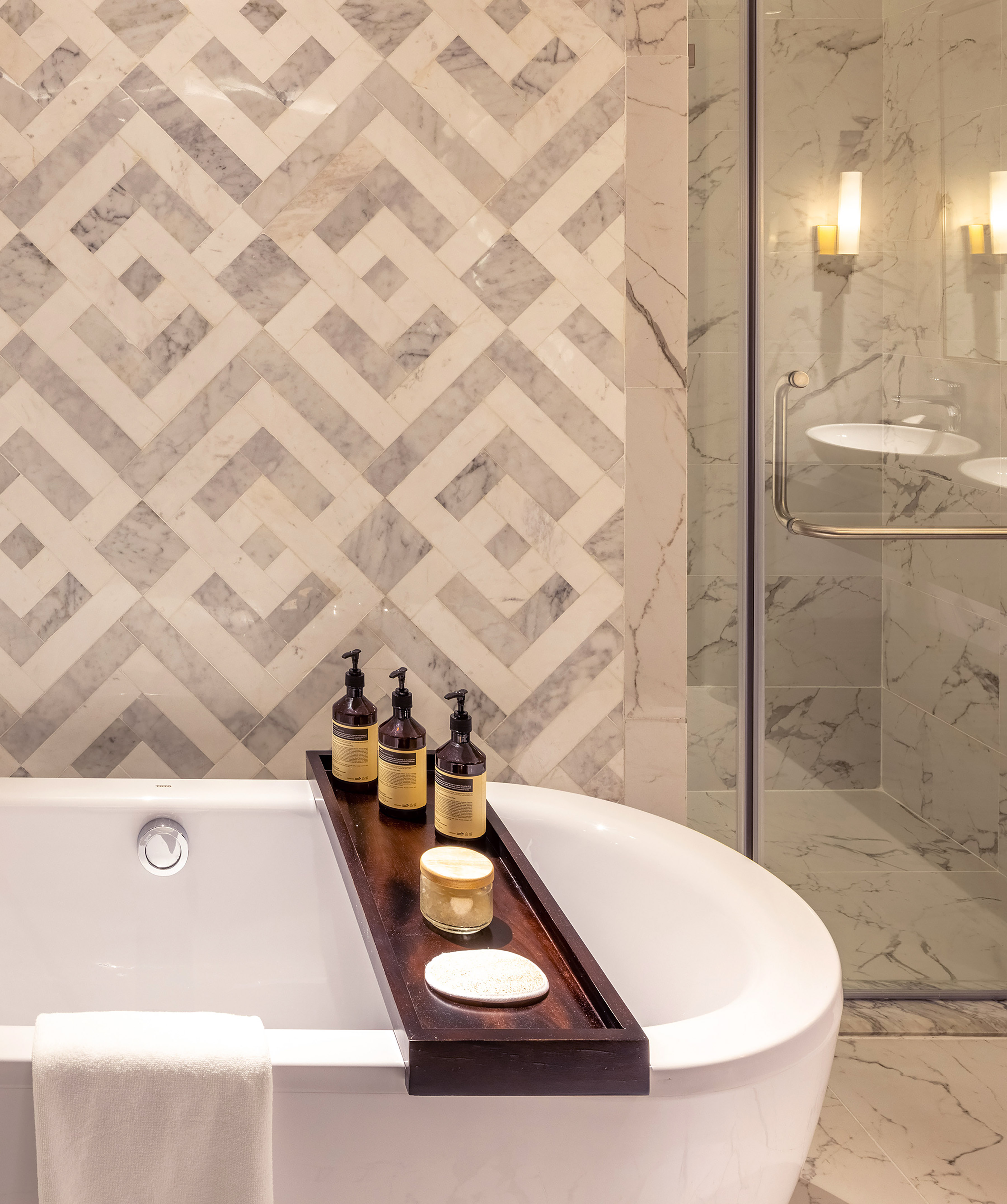 Freestanding tub, bath caddy with toiletries, and geometric marble tile wall.
