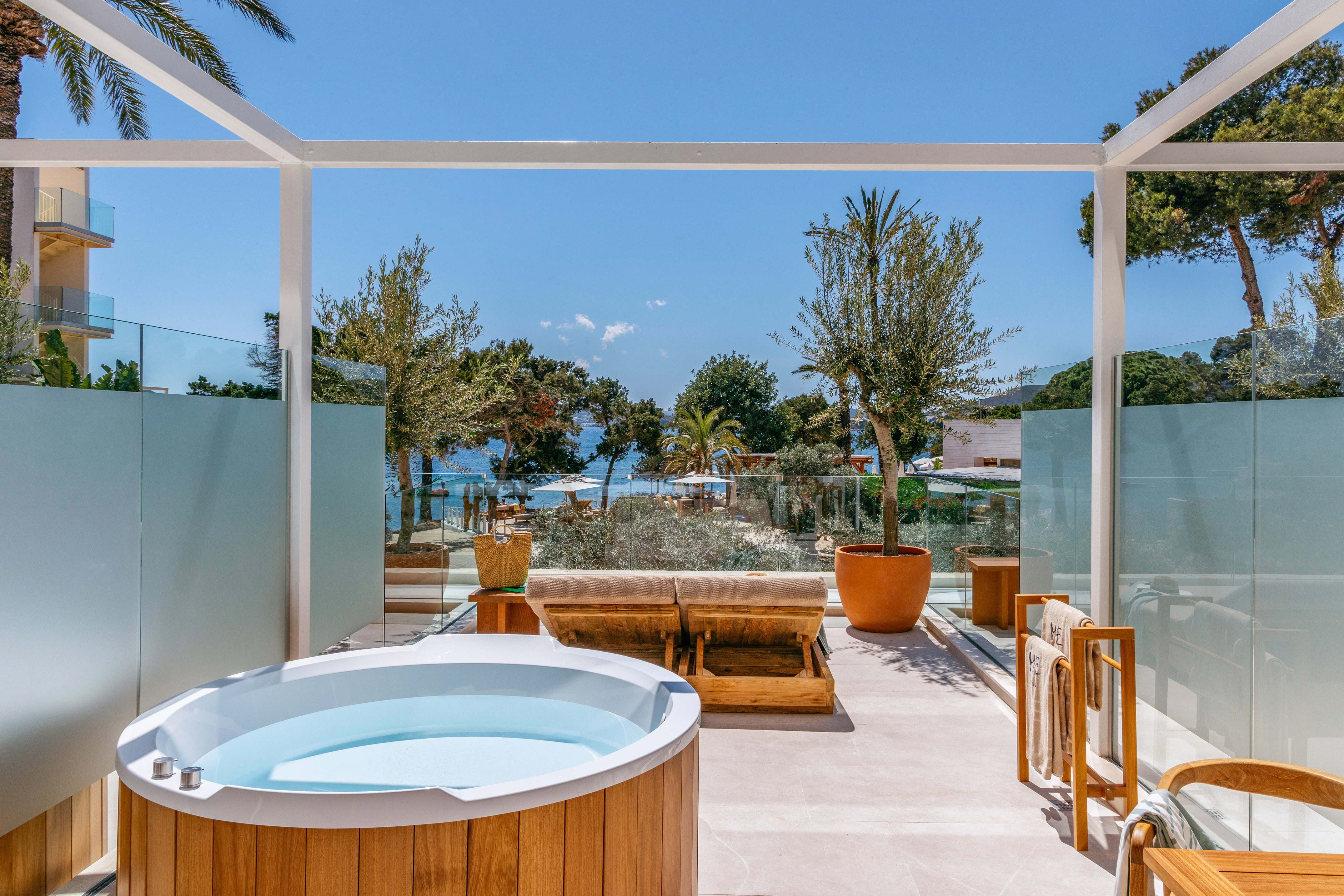 Luxury terrace with wooden hot tub, sunbeds, and ocean view.