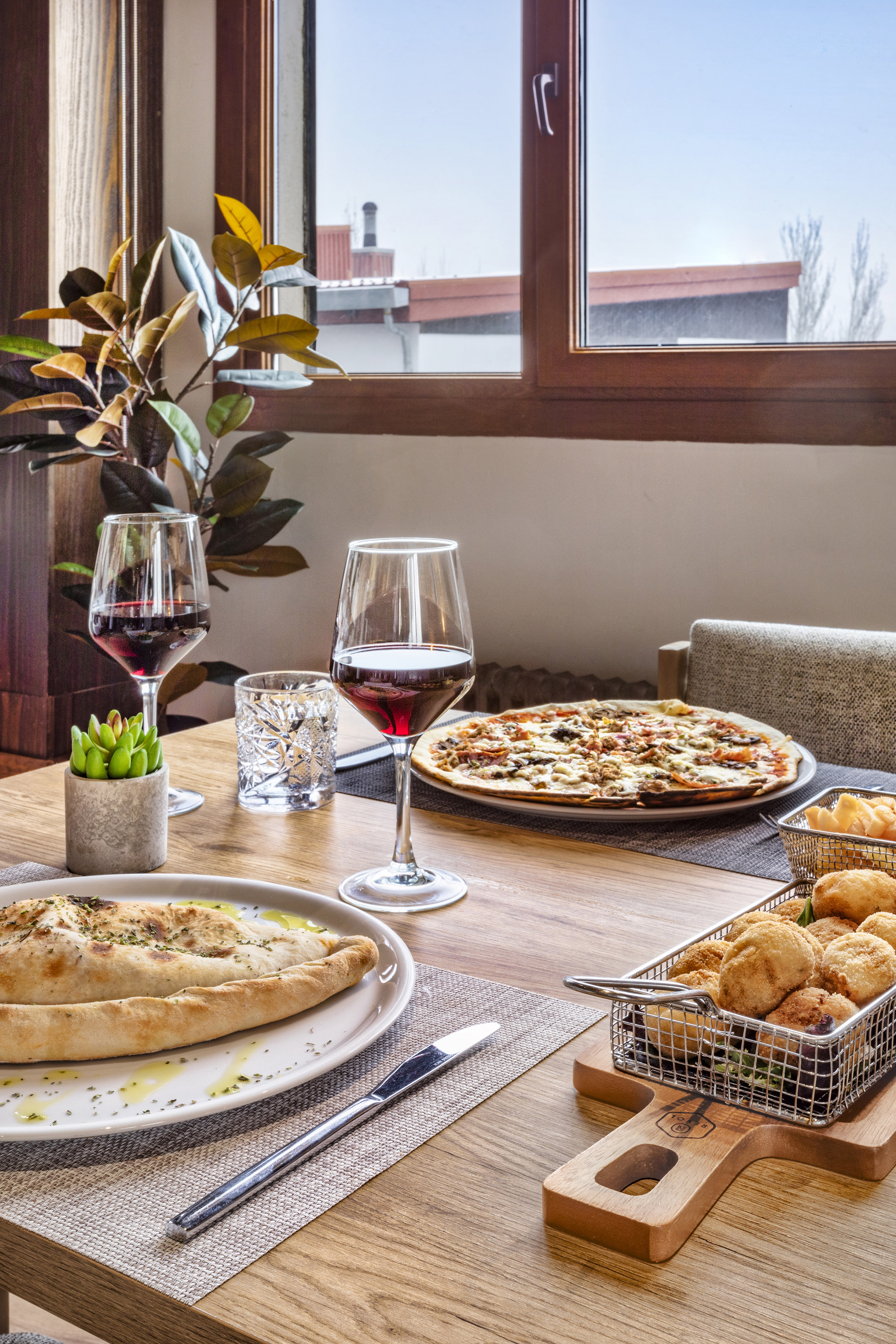 Restaurant table with pizza, calzone, fried appetizers, and red wine.