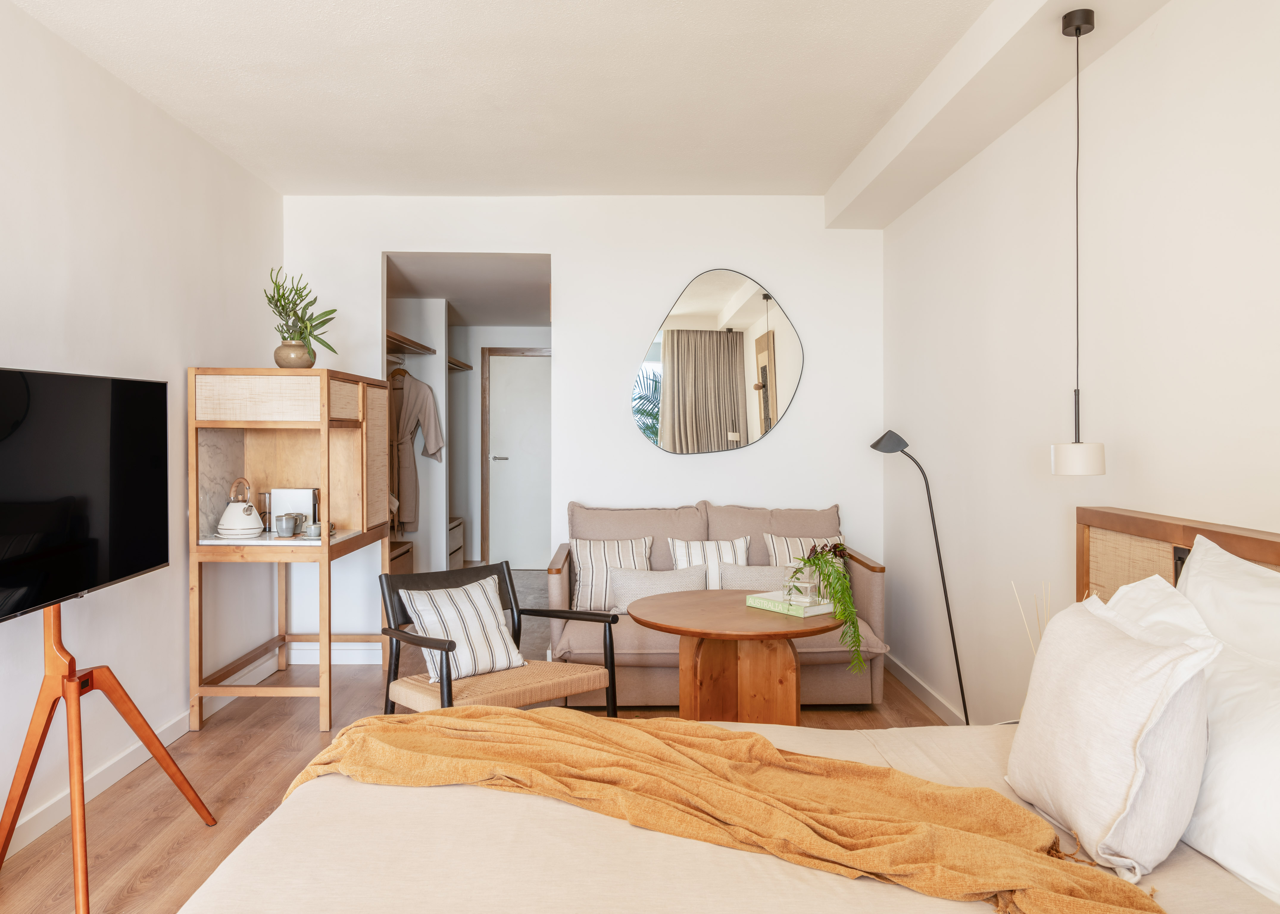 Modern hotel suite with bed, sofa, natural wood furniture, and minimalist design.