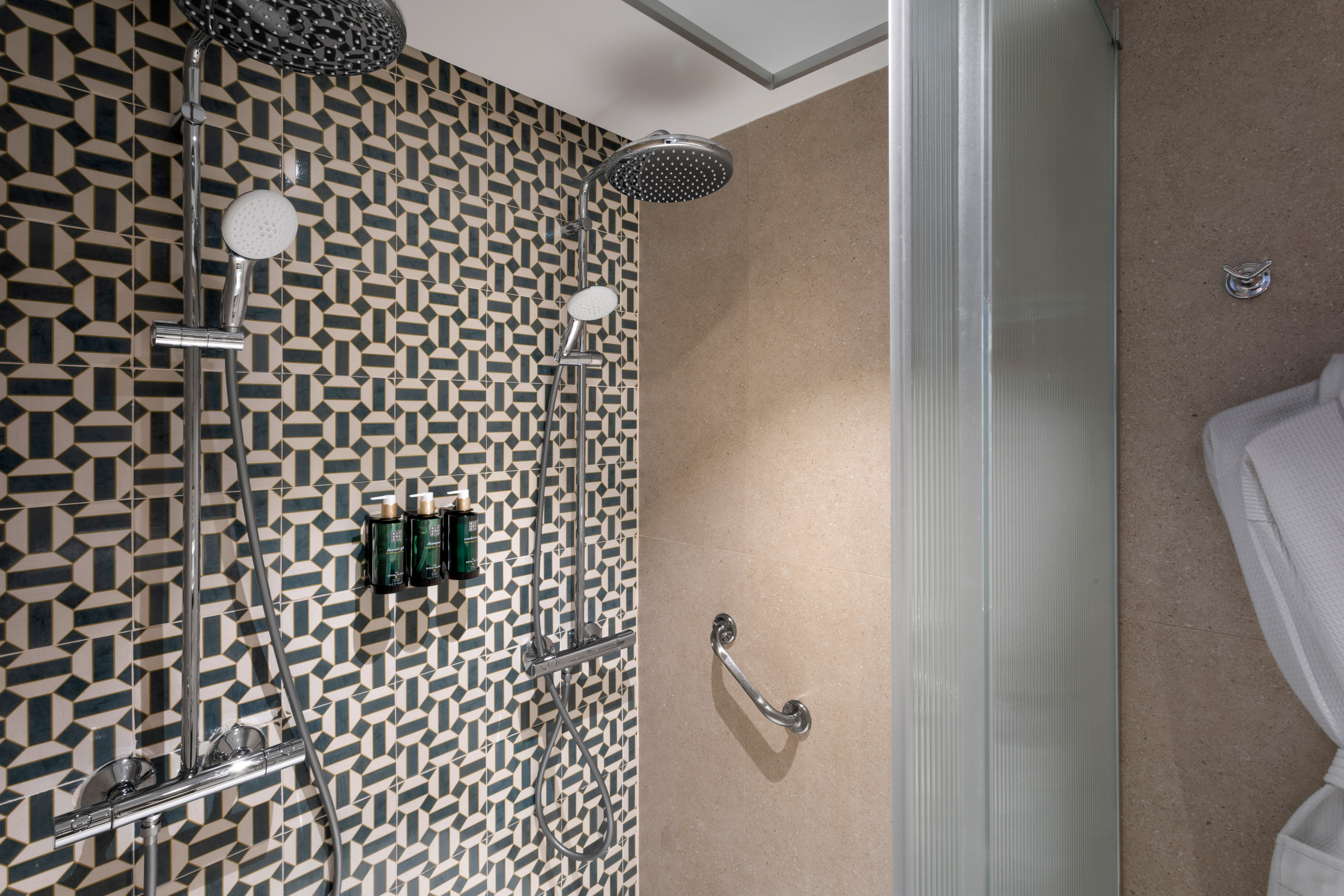 Modern shower with geometric tiled wall, dual heads, and accessibility grab bar.