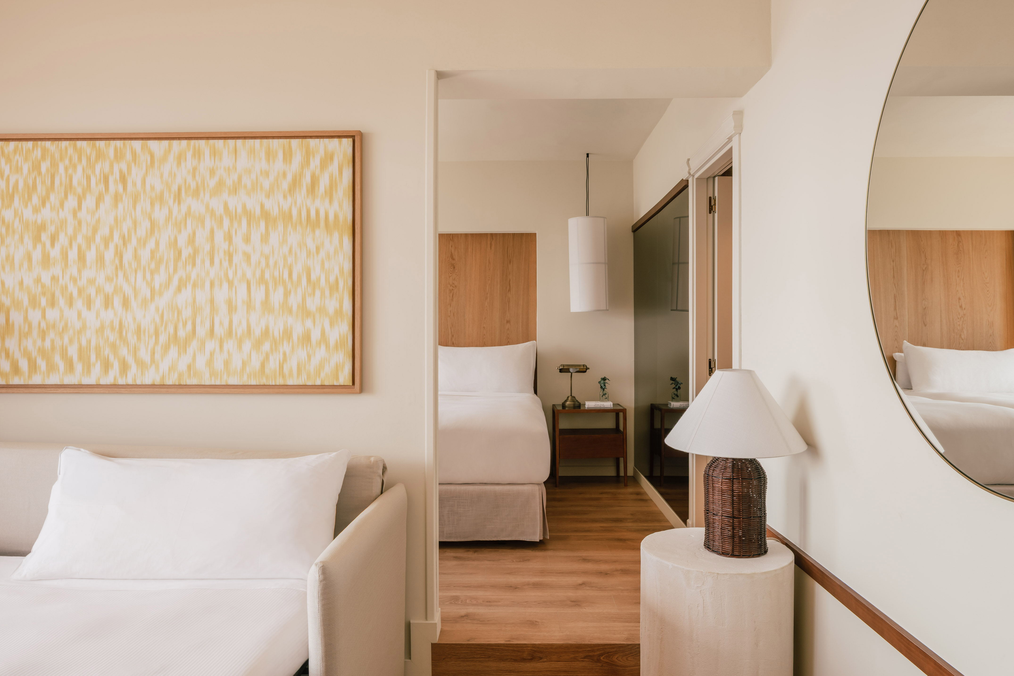 Bright modern hotel suite with sofa, bedroom, and decorative mirror.