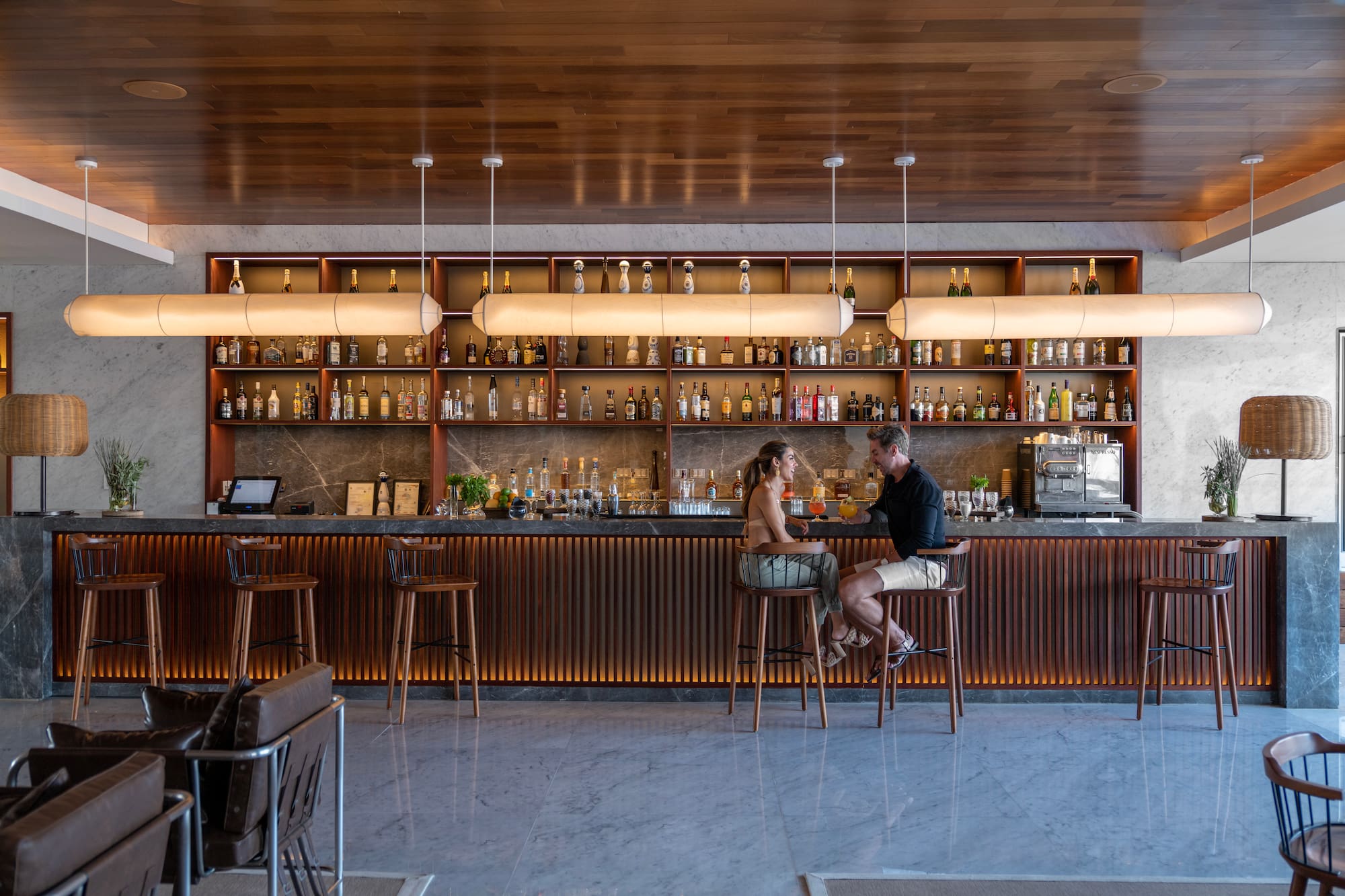 Couple enjoying cocktails at a modern hotel bar with a stylish liquor display.