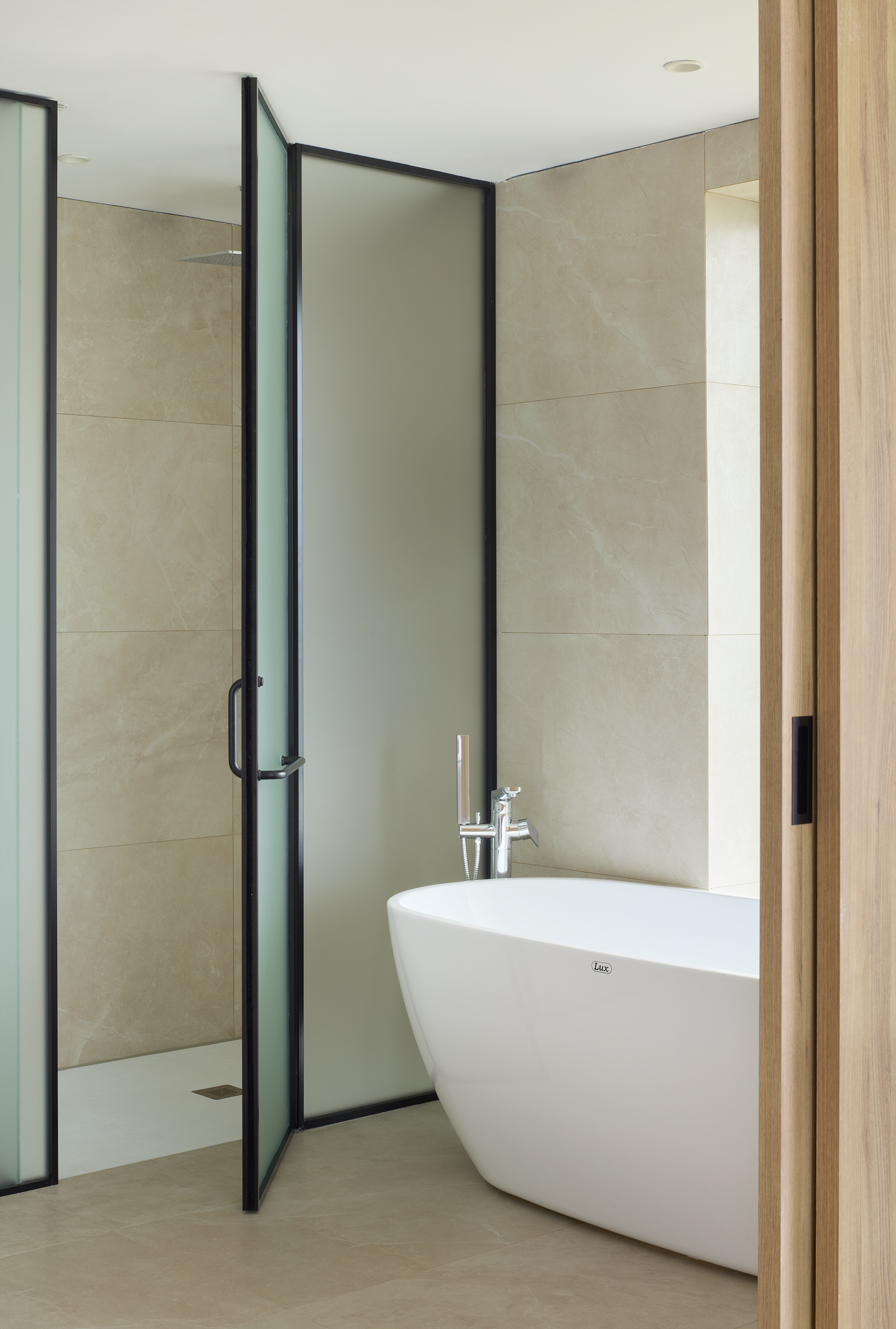 Modern bathroom with freestanding tub, black-framed glass shower, marble walls.