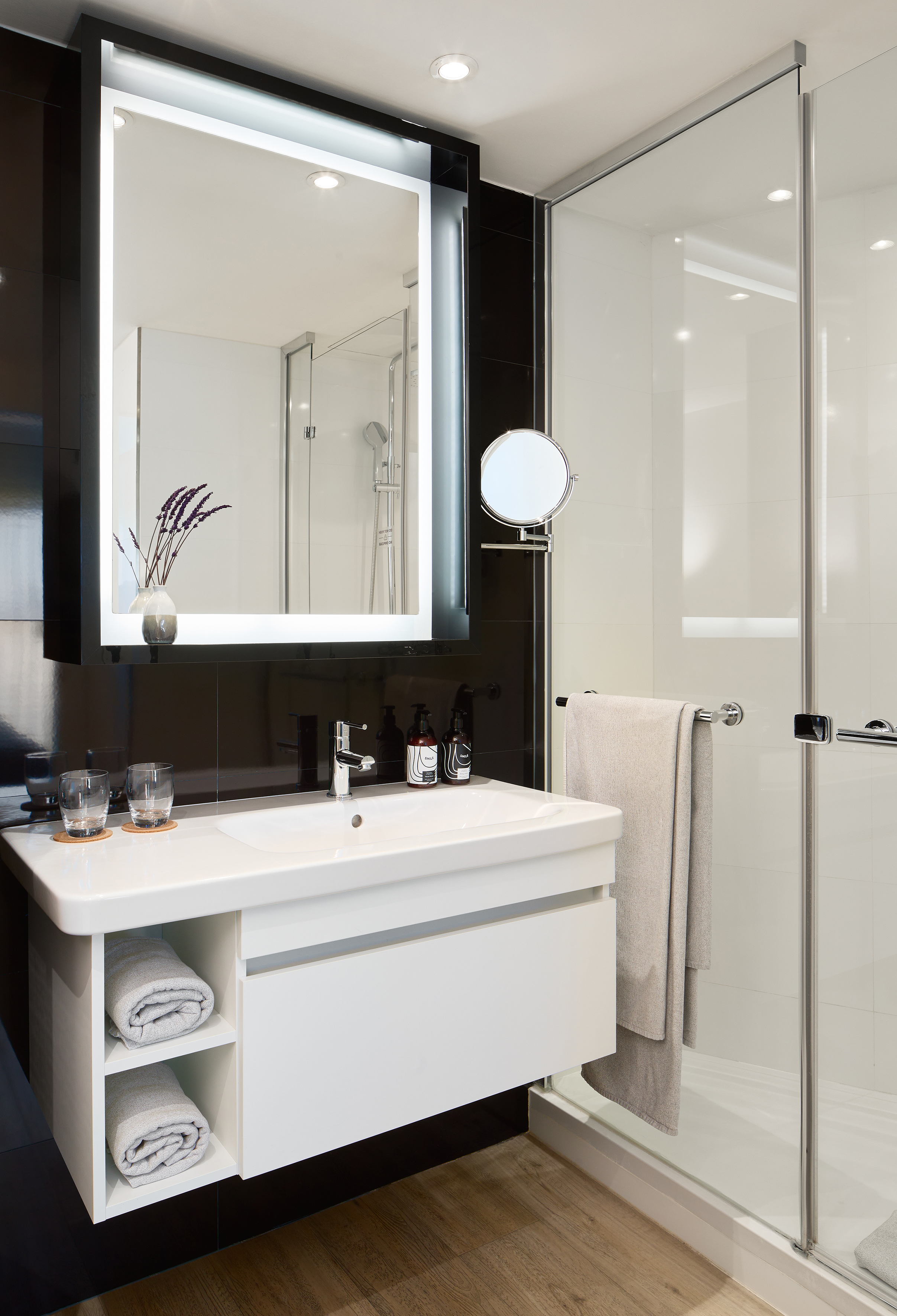 Modern bathroom with white vanity, illuminated mirror, and glass shower.