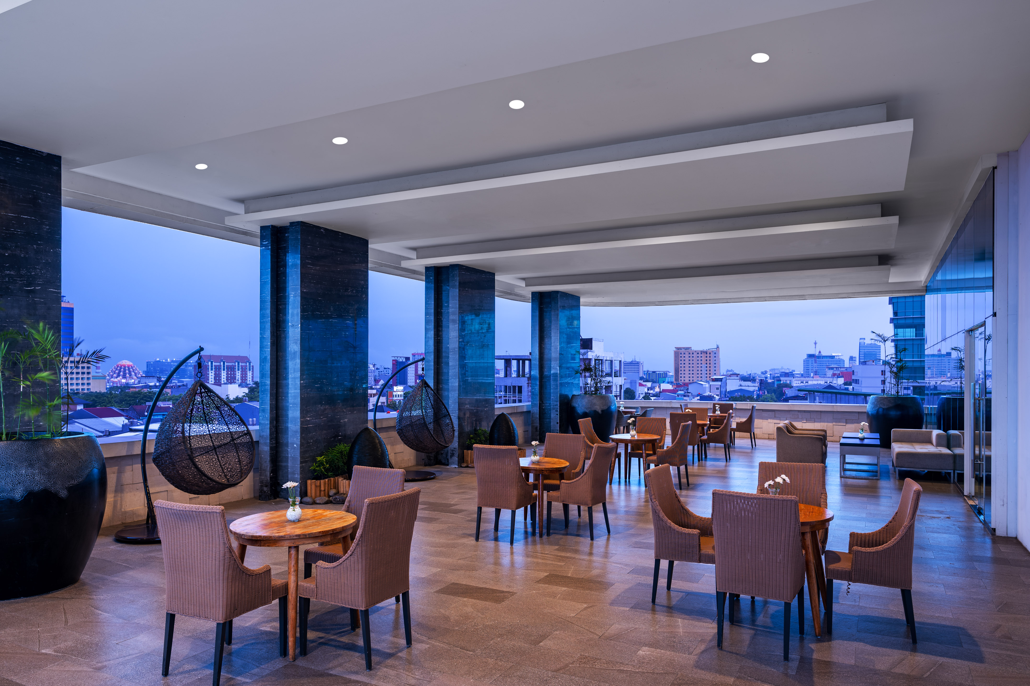 Stylish outdoor rooftop lounge and dining area with city skyline view at dusk.