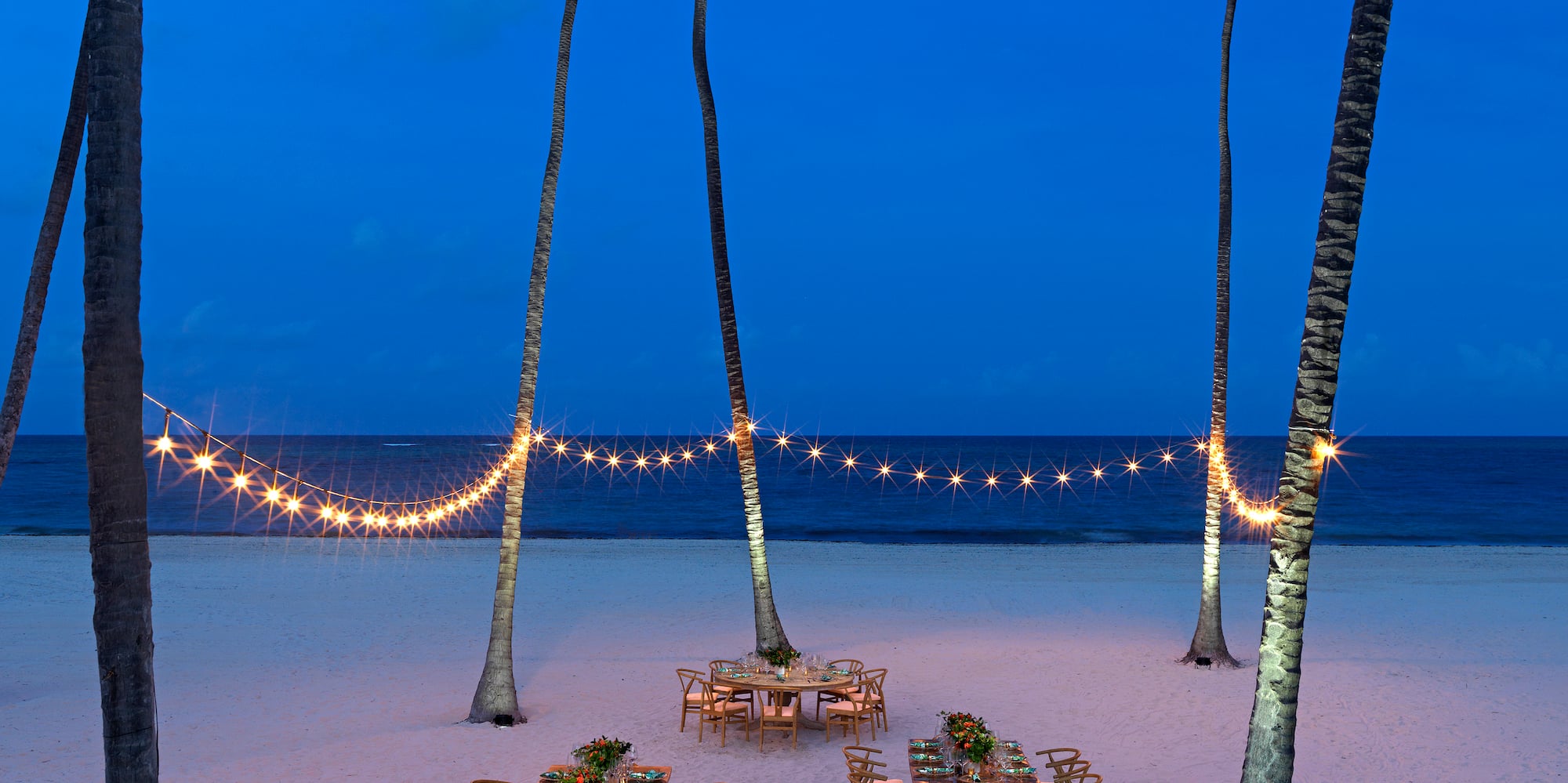 a table set up on a beach with palm trees and string lights