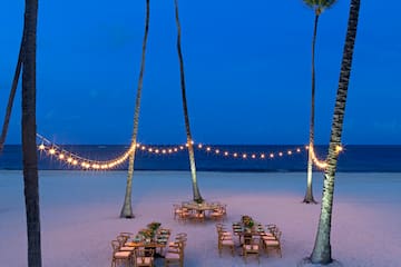 a table set up on a beach with palm trees and string lights