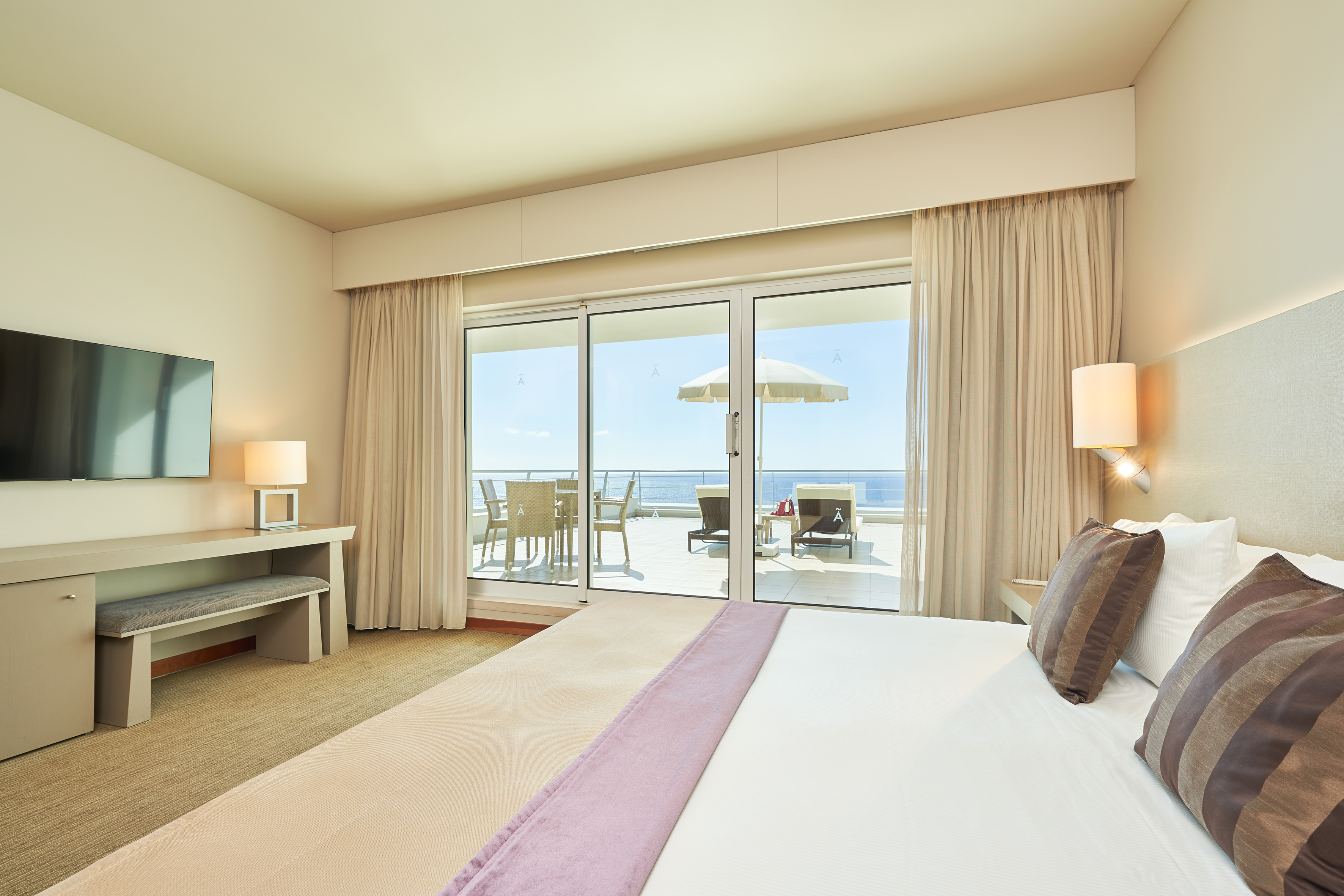 Hotel bedroom with ocean view balcony, outdoor table, chairs, and loungers.