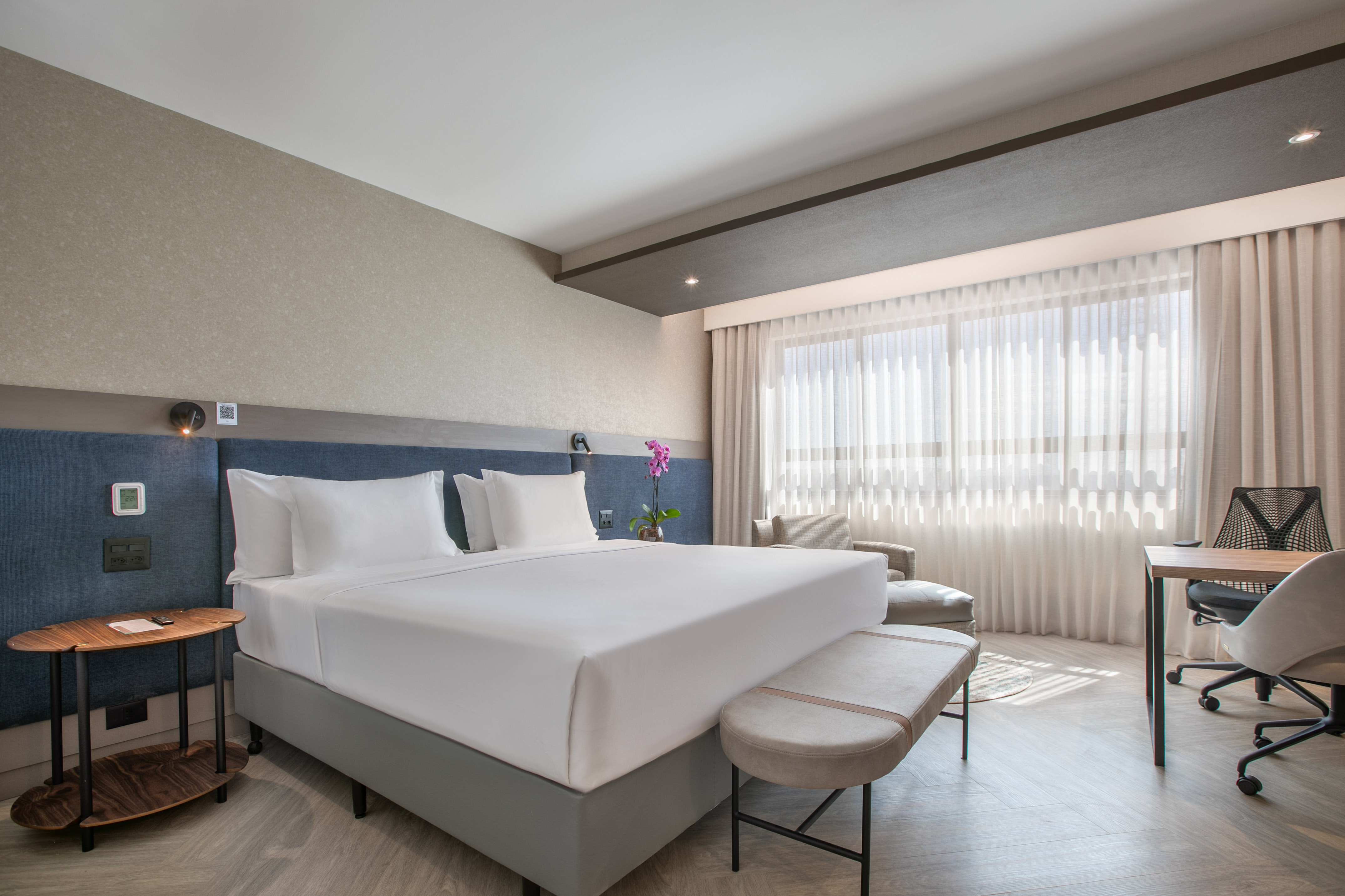Contemporary hotel bedroom suite with king bed, desk area, and natural light.