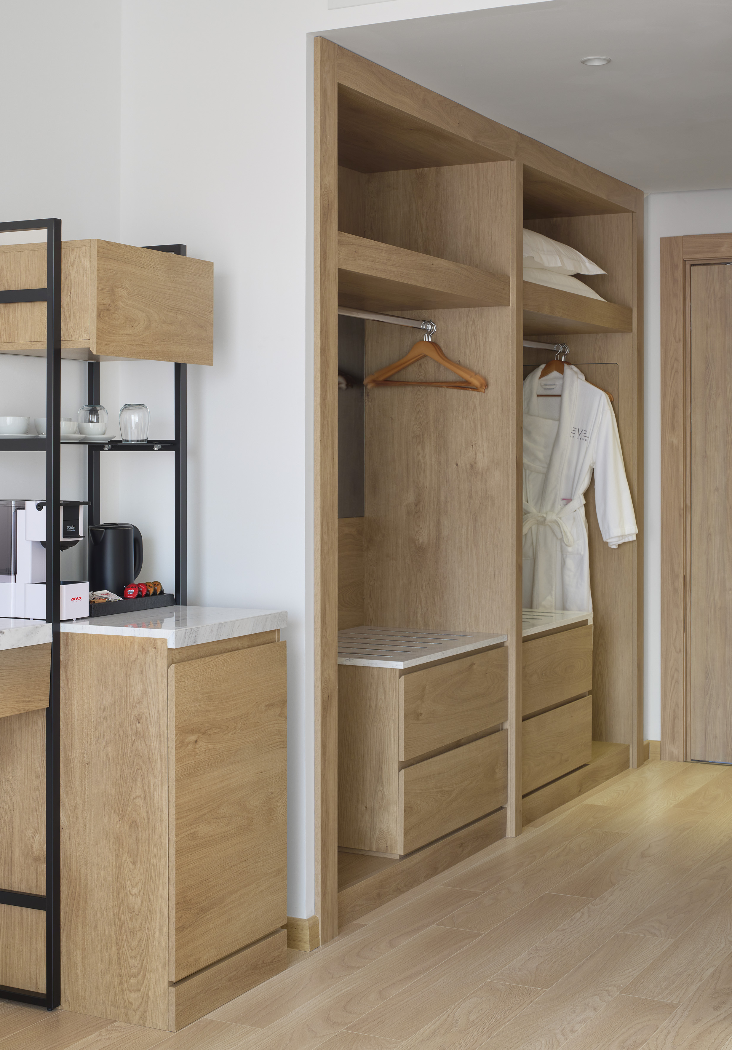 Sleek wooden wardrobe, hotel robe, pillows, and integrated coffee bar area.