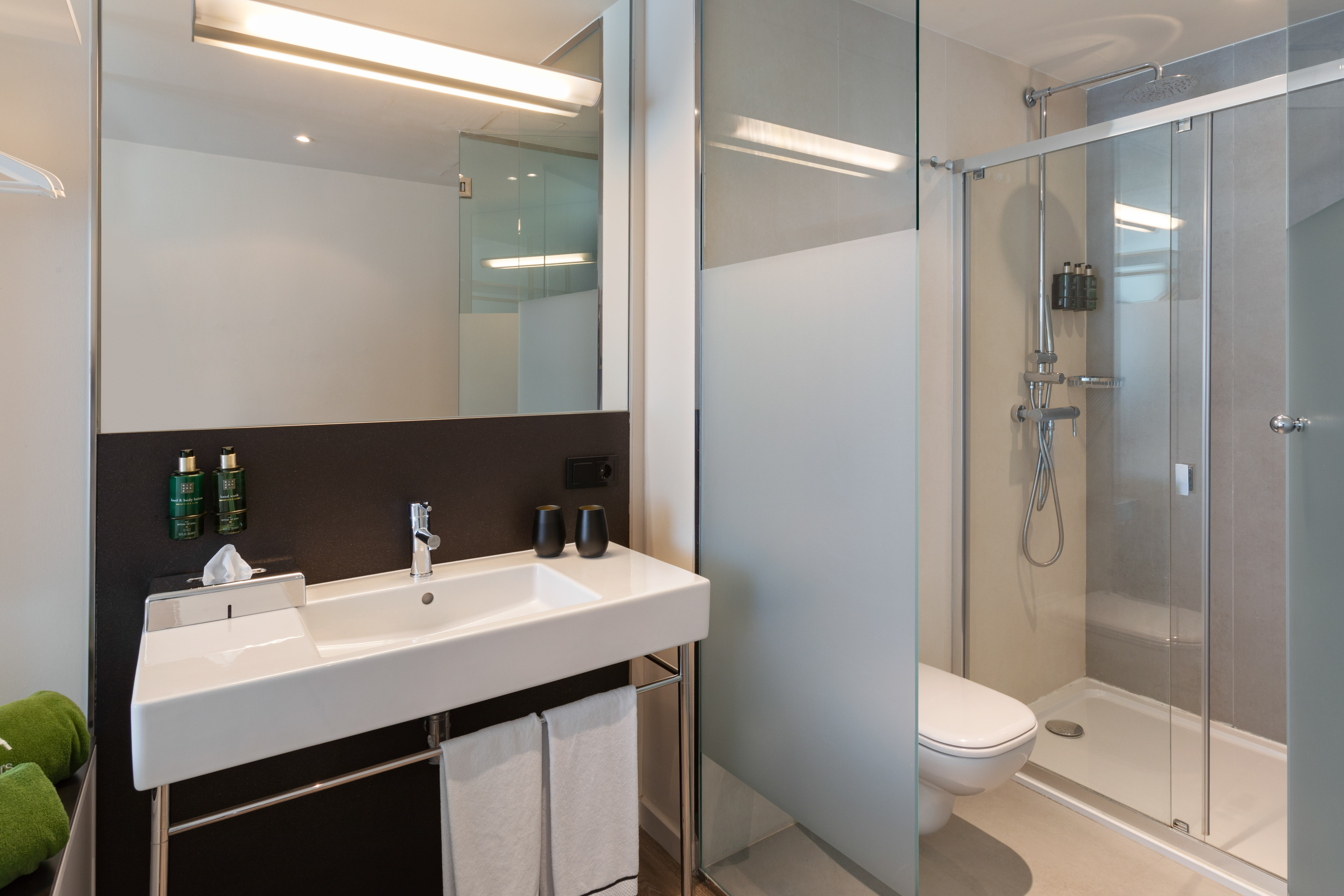Modern hotel bathroom with white sink, illuminated mirror, and sleek glass shower.