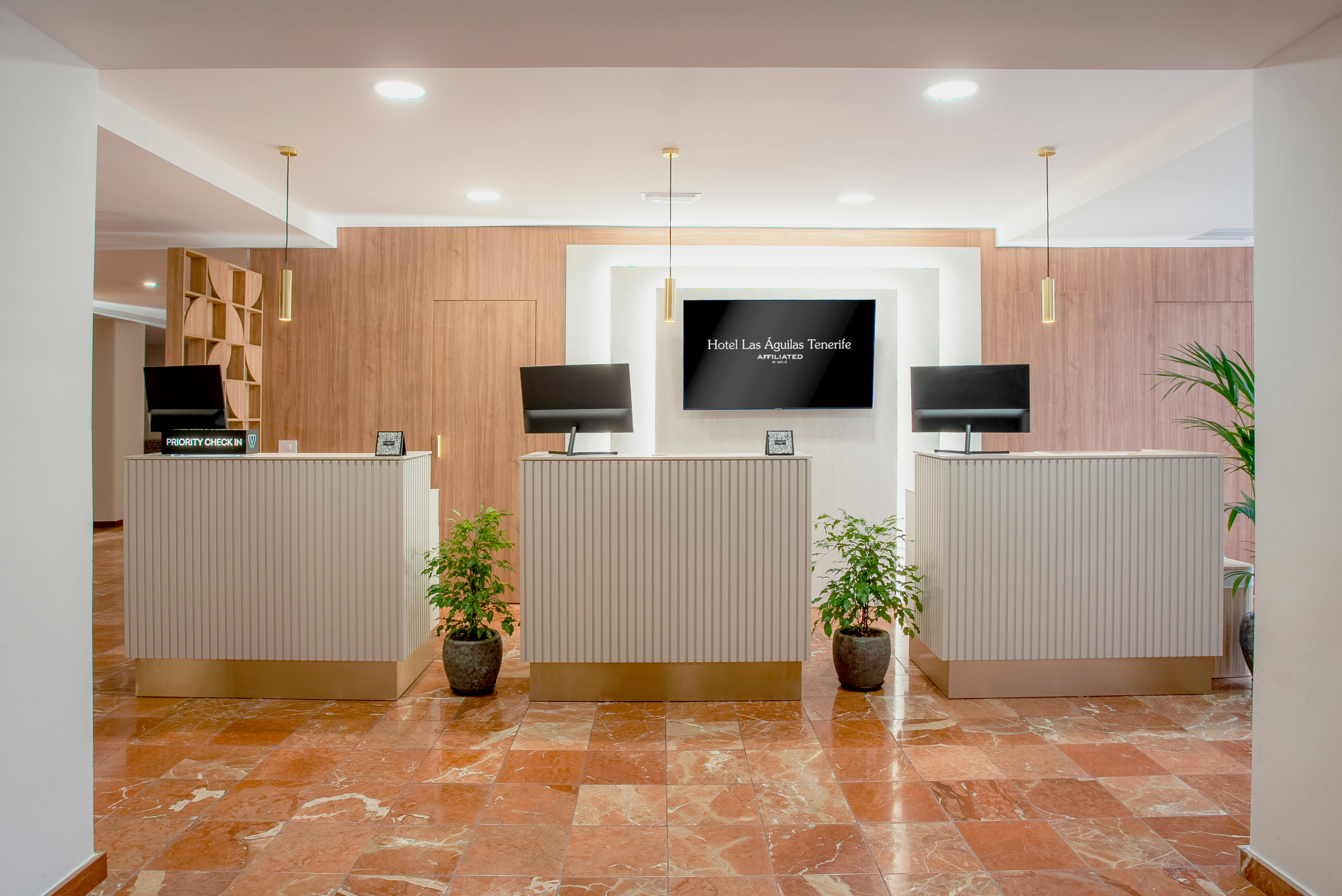 Hotel Las Águilas Tenerife modern lobby with three reception desks, brand TV, and plants.