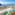 Balcony ocean view: green chair, coastal town, blue sea, cliffs.