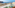 Balcony ocean view: green chair, coastal town, blue sea, cliffs.