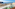 Balcony ocean view: green chair, coastal town, blue sea, cliffs.