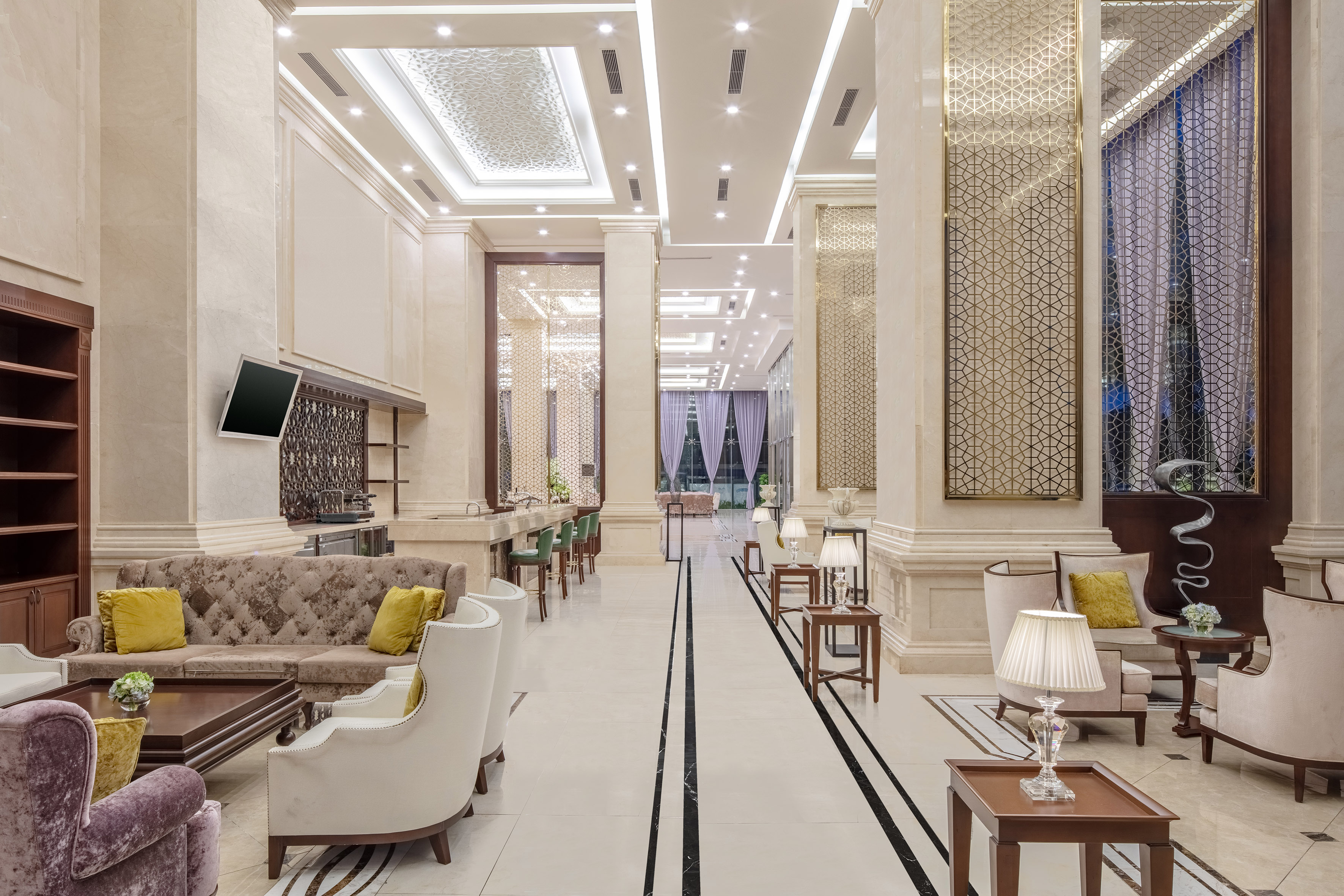 Grand hotel lobby with elegant seating, patterned gold screens, and marble floor.