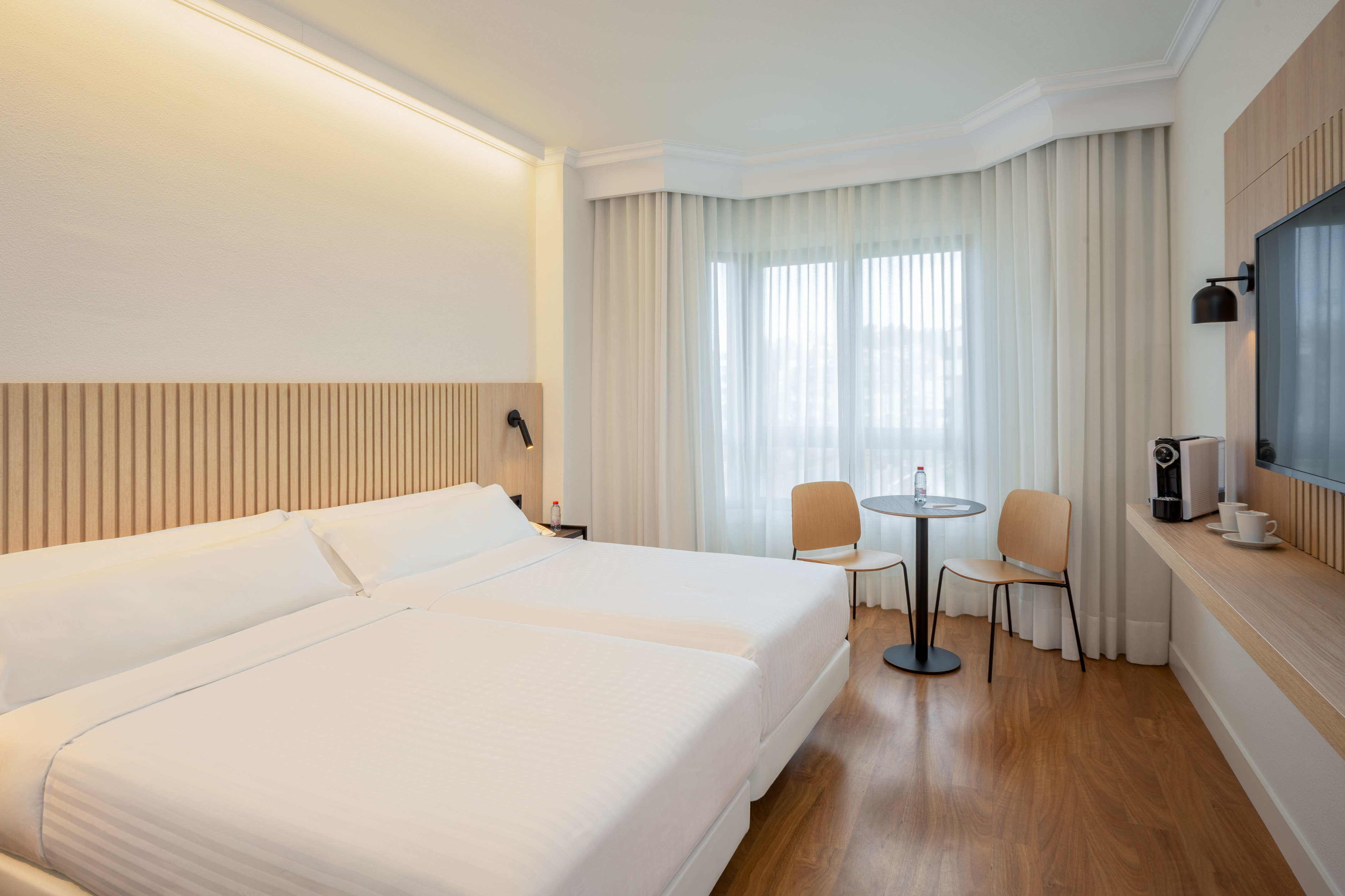 Modern hotel room with twin beds, wood accents, a window, and coffee maker.