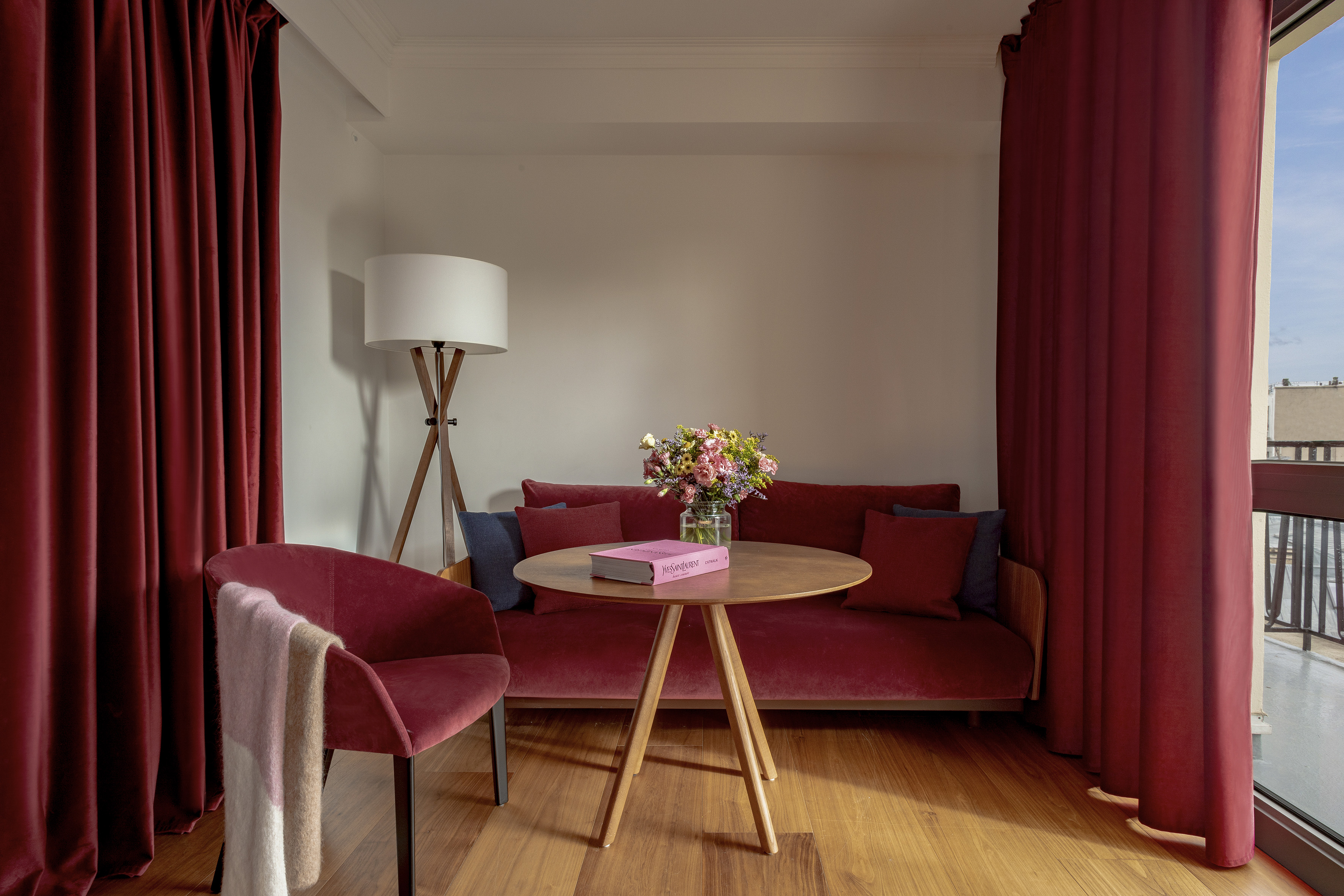Cozy room with red velvet sofa, wooden table, flowers, and modern lamp.