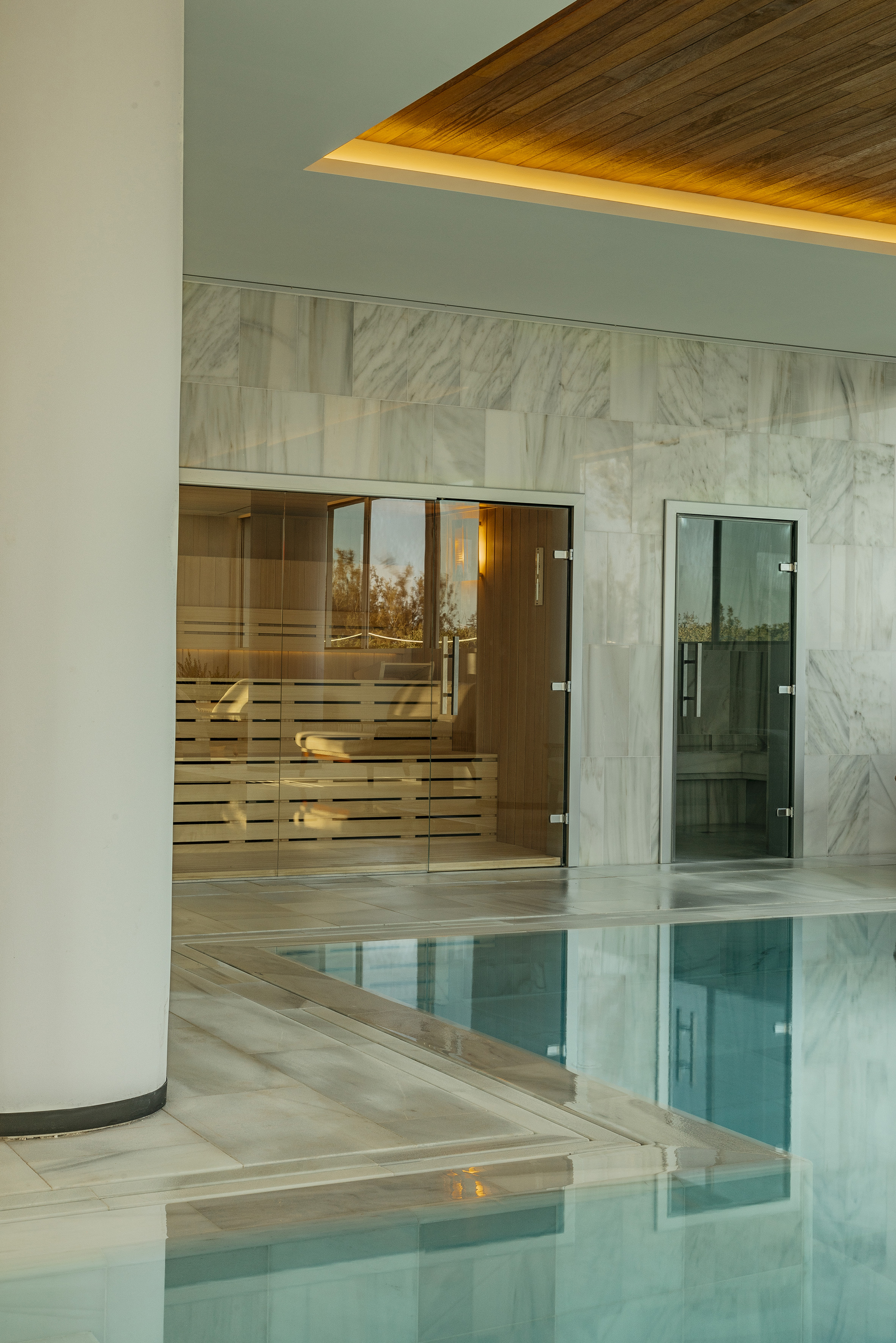 Luxury spa indoor pool, glass sauna, and marble interior with wood ceiling.