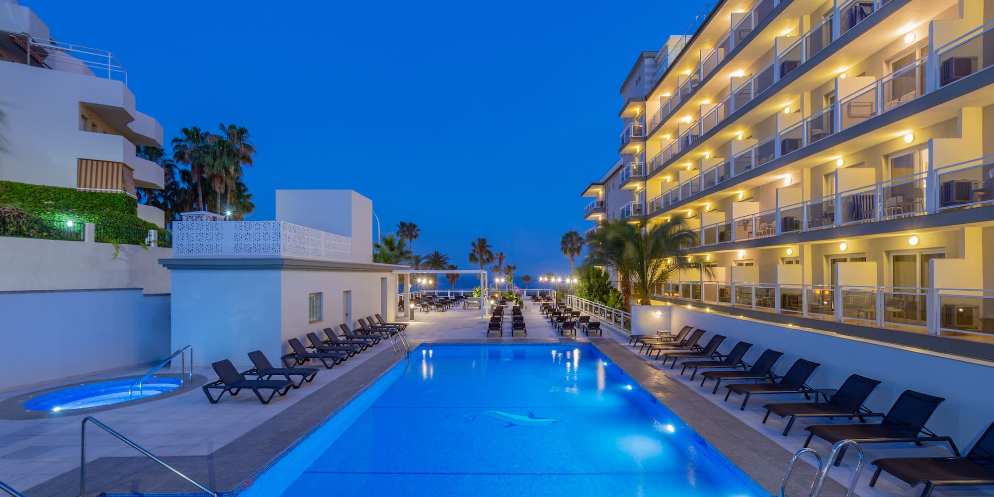 a pool with chairs and a building with palm trees