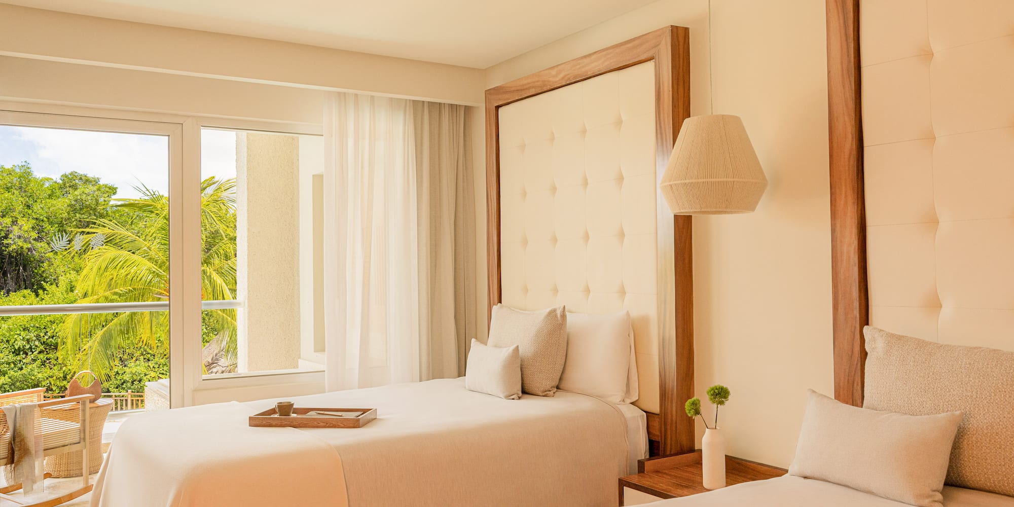 Modern hotel room with two twin beds, wood headboards, and lush tropical view.