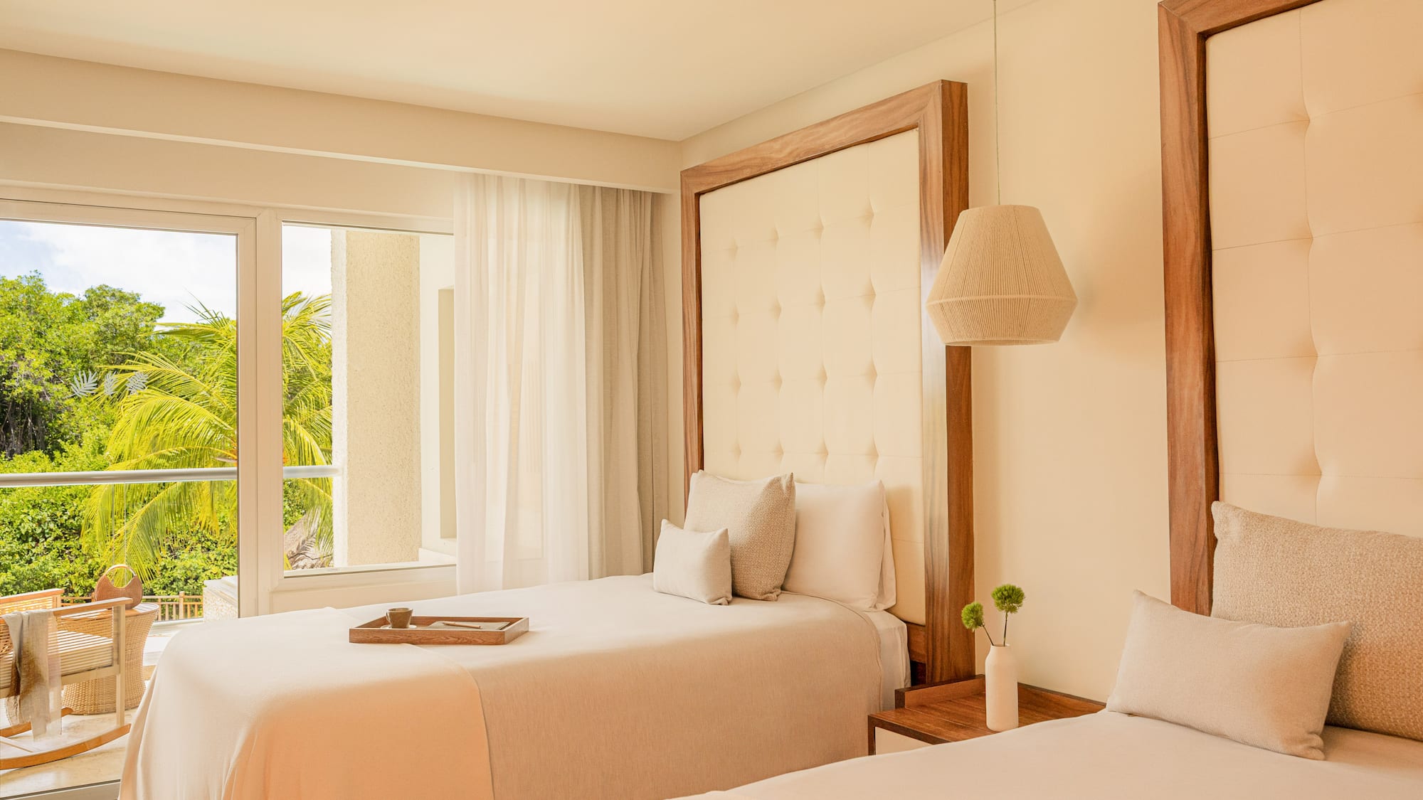 Modern hotel room with two twin beds, wood headboards, and lush tropical view.