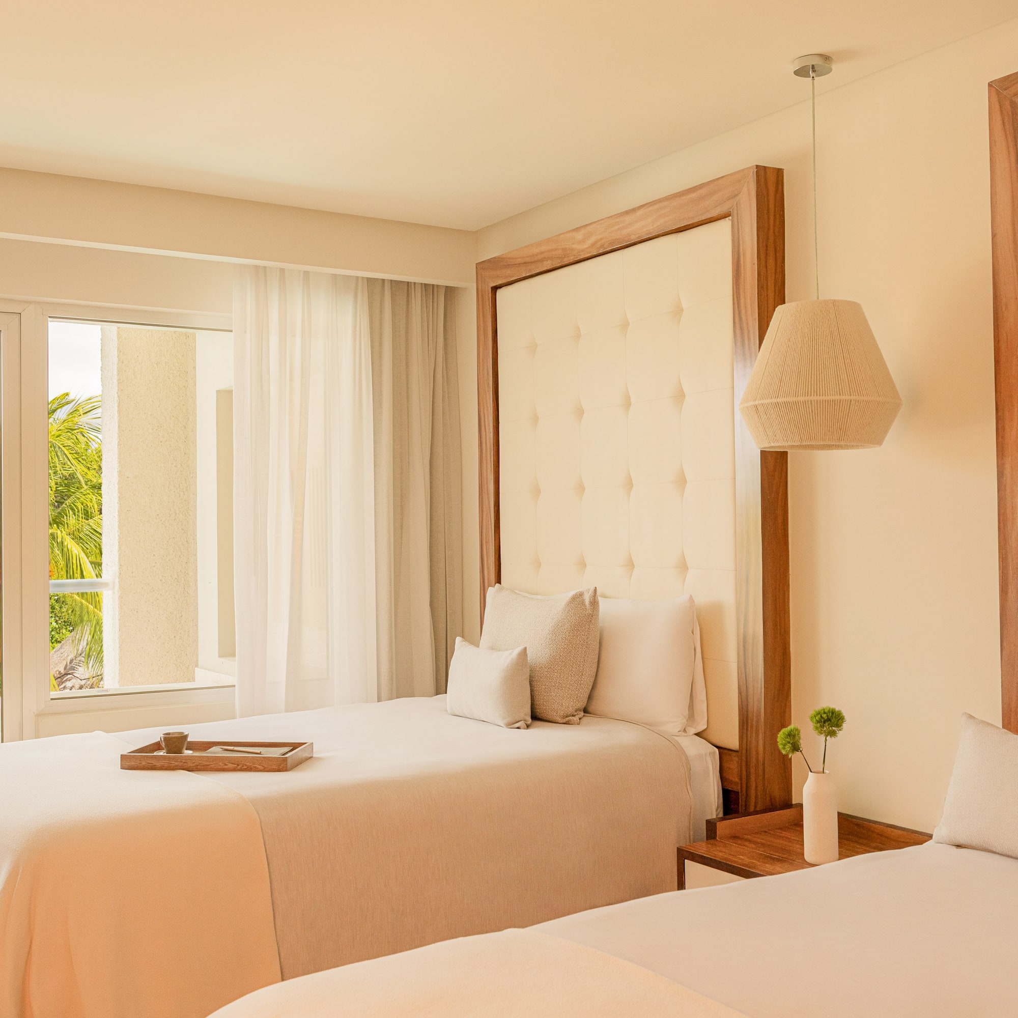 Neutral twin bedroom with tufted headboards and a lush tropical balcony view.