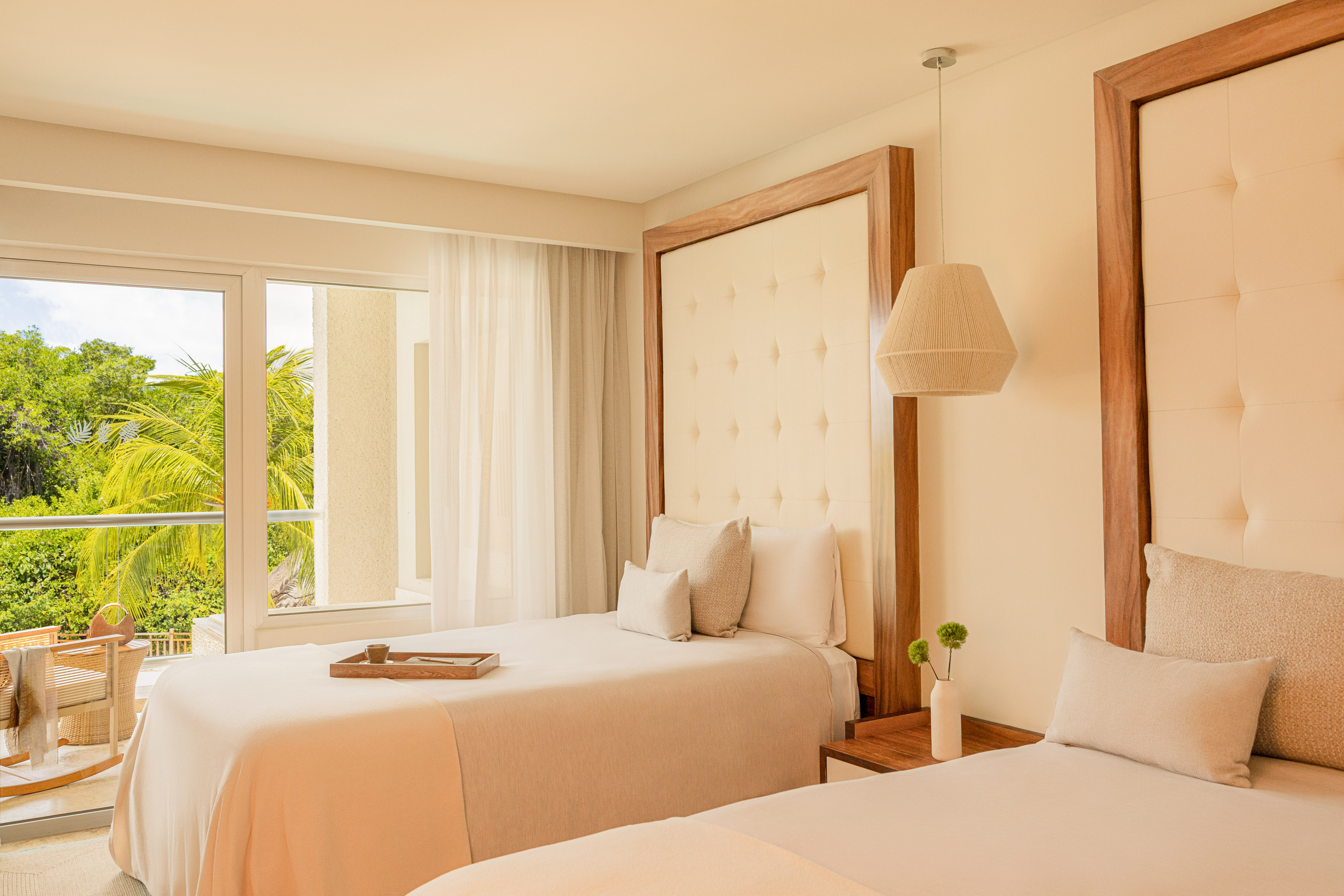 Modern hotel room with two twin beds, wood headboards, and lush tropical view.