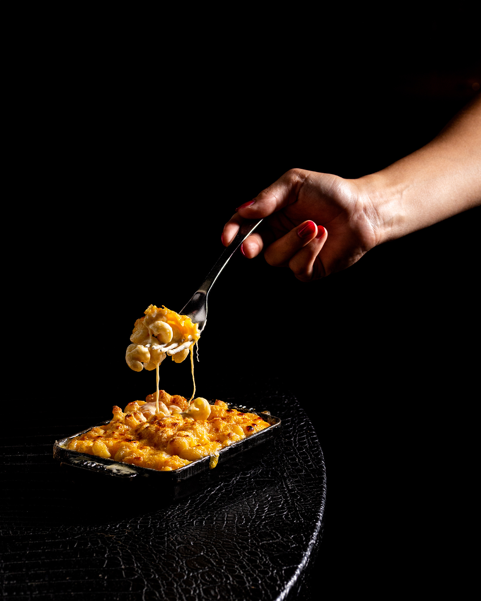 Fork lifting hot, cheesy mac and cheese from a dark pan. Delicious comfort food.