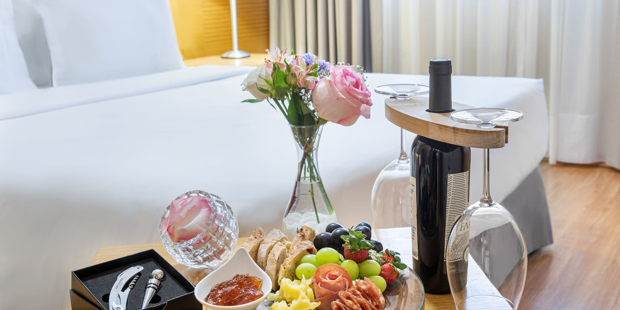 Romantic hotel room with charcuterie board, wine, and fresh flowers.