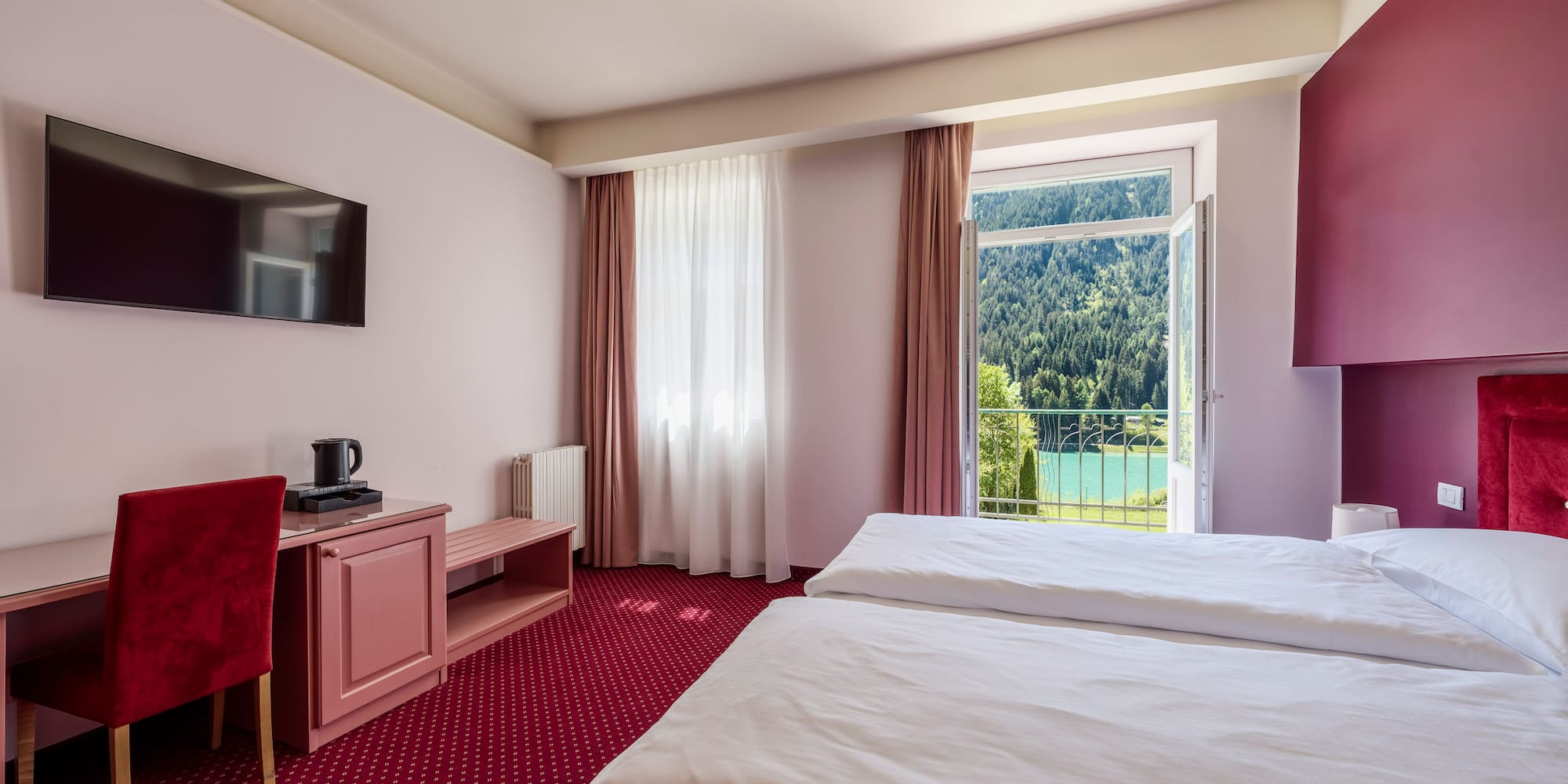 Hotel bedroom with twin beds, red carpet, and balcony lake view.