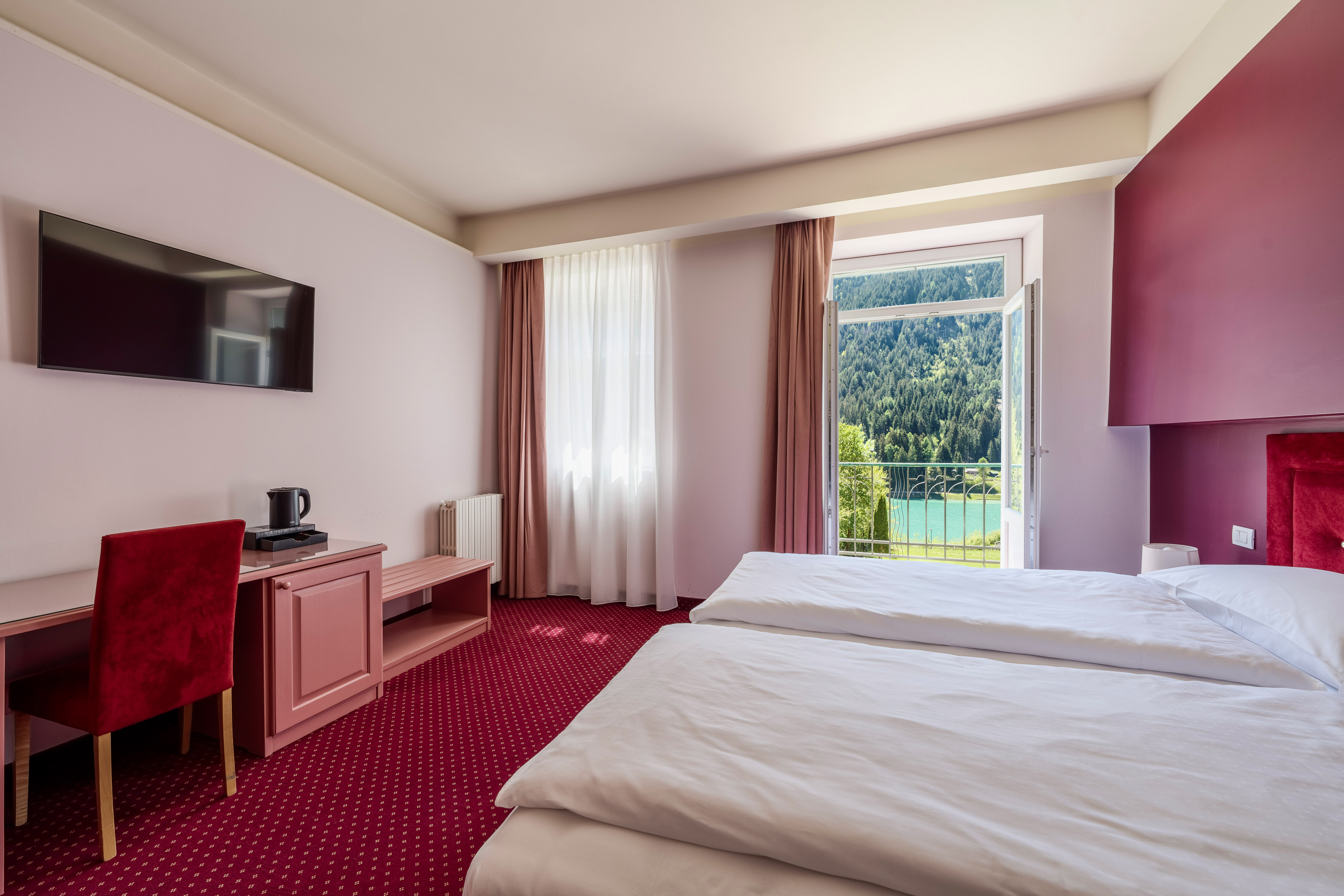 Hotel bedroom with twin beds, red carpet, and balcony lake view.