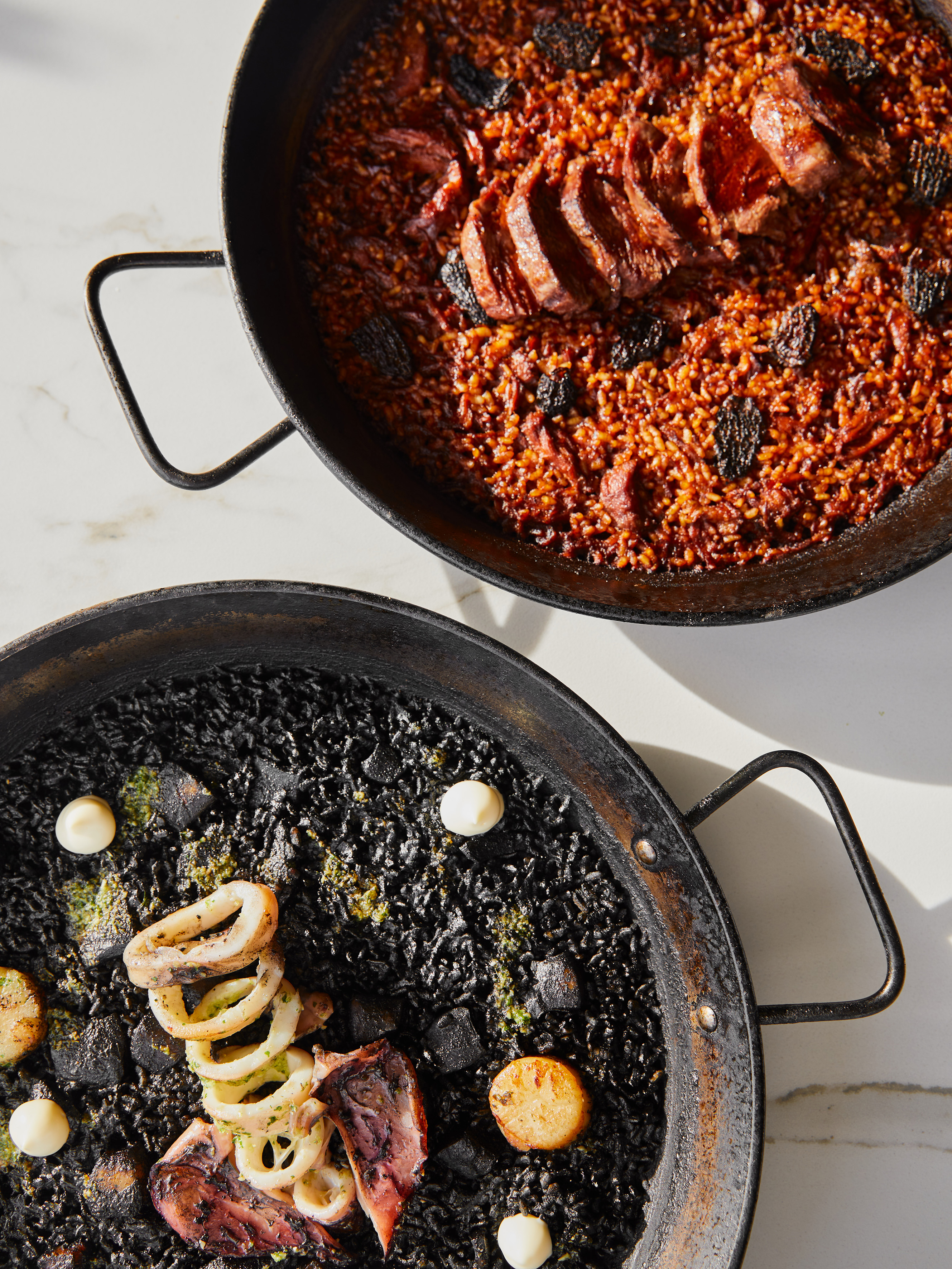 Two paella pans: savory red meat rice and black squid ink seafood rice.