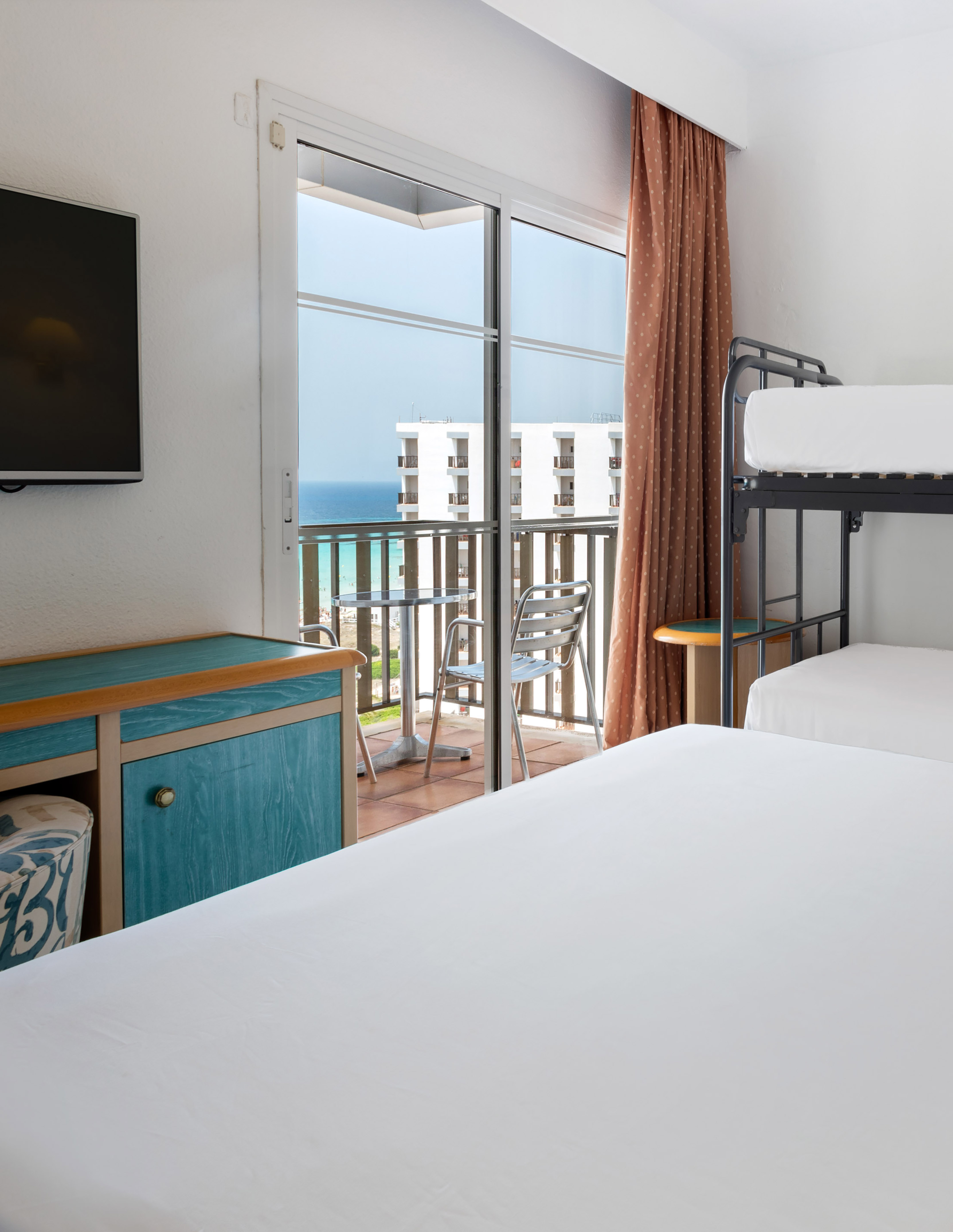 Hotel room with bunk beds, sea view balcony, and flat-screen TV.
