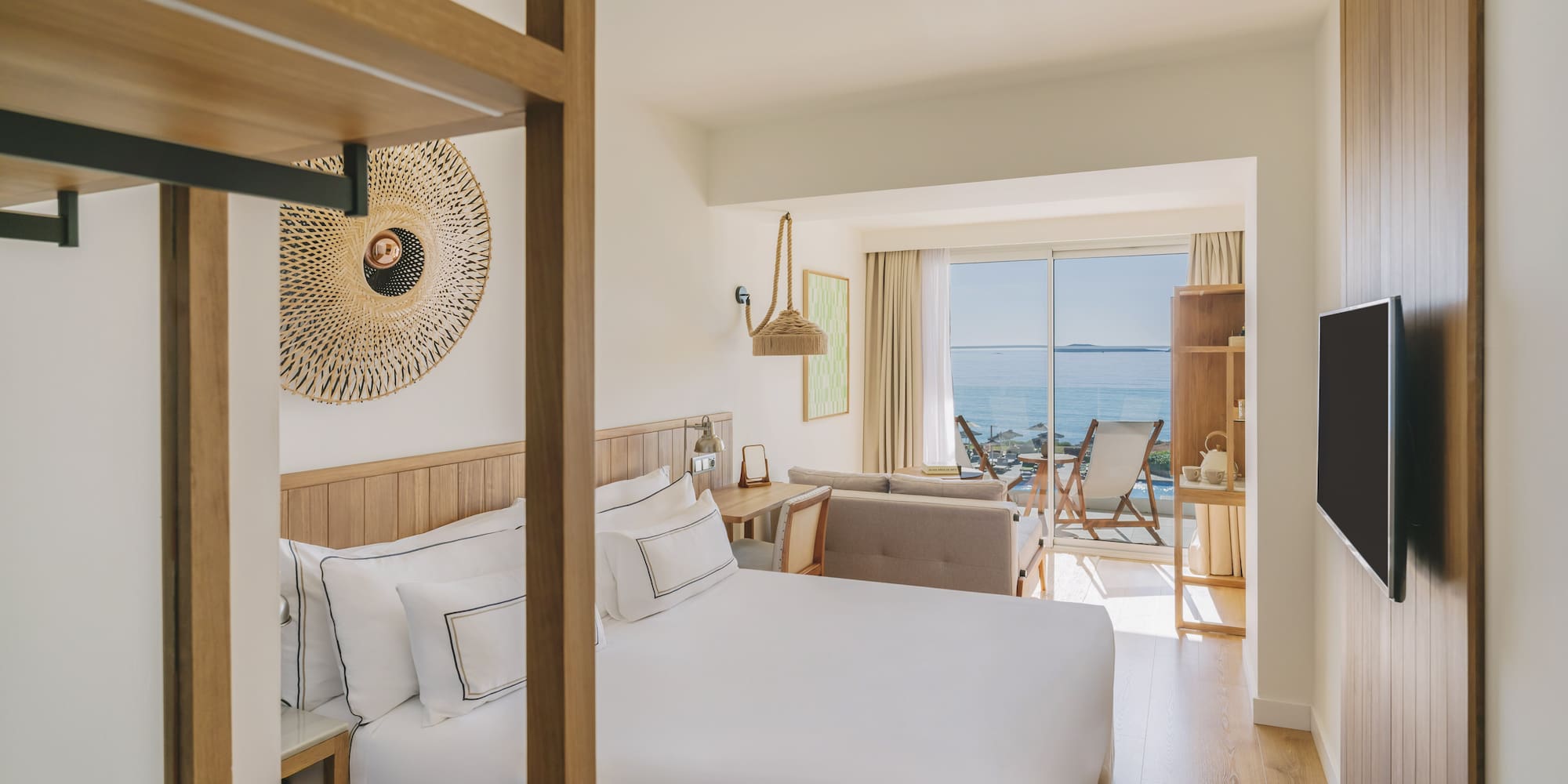 Modern hotel room with king bed, ocean view balcony, and wood decor.